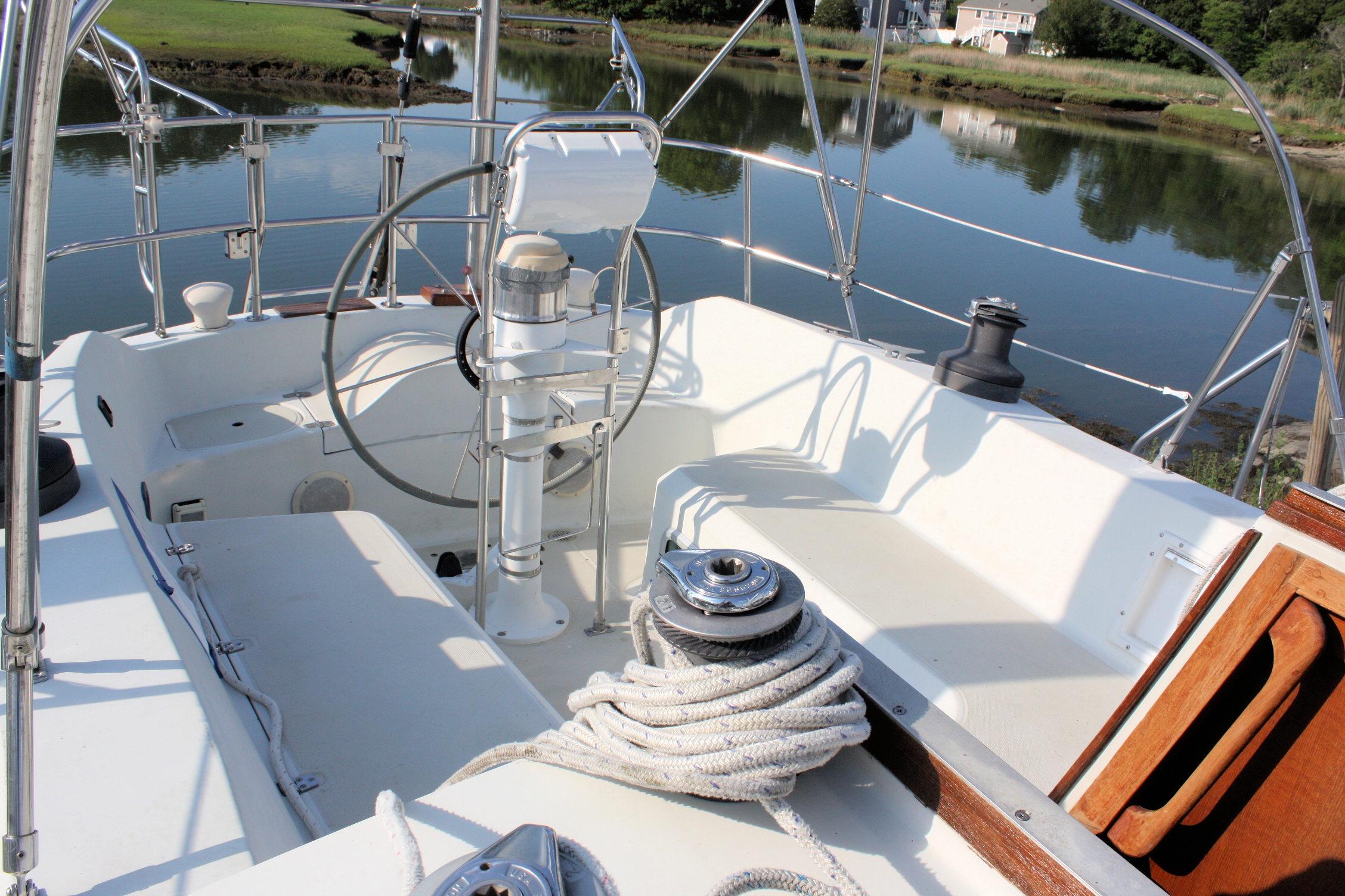 Cockpit of 1987 Ericson 38-200 sailboat with steering wheel and winch, docked by calm water.
