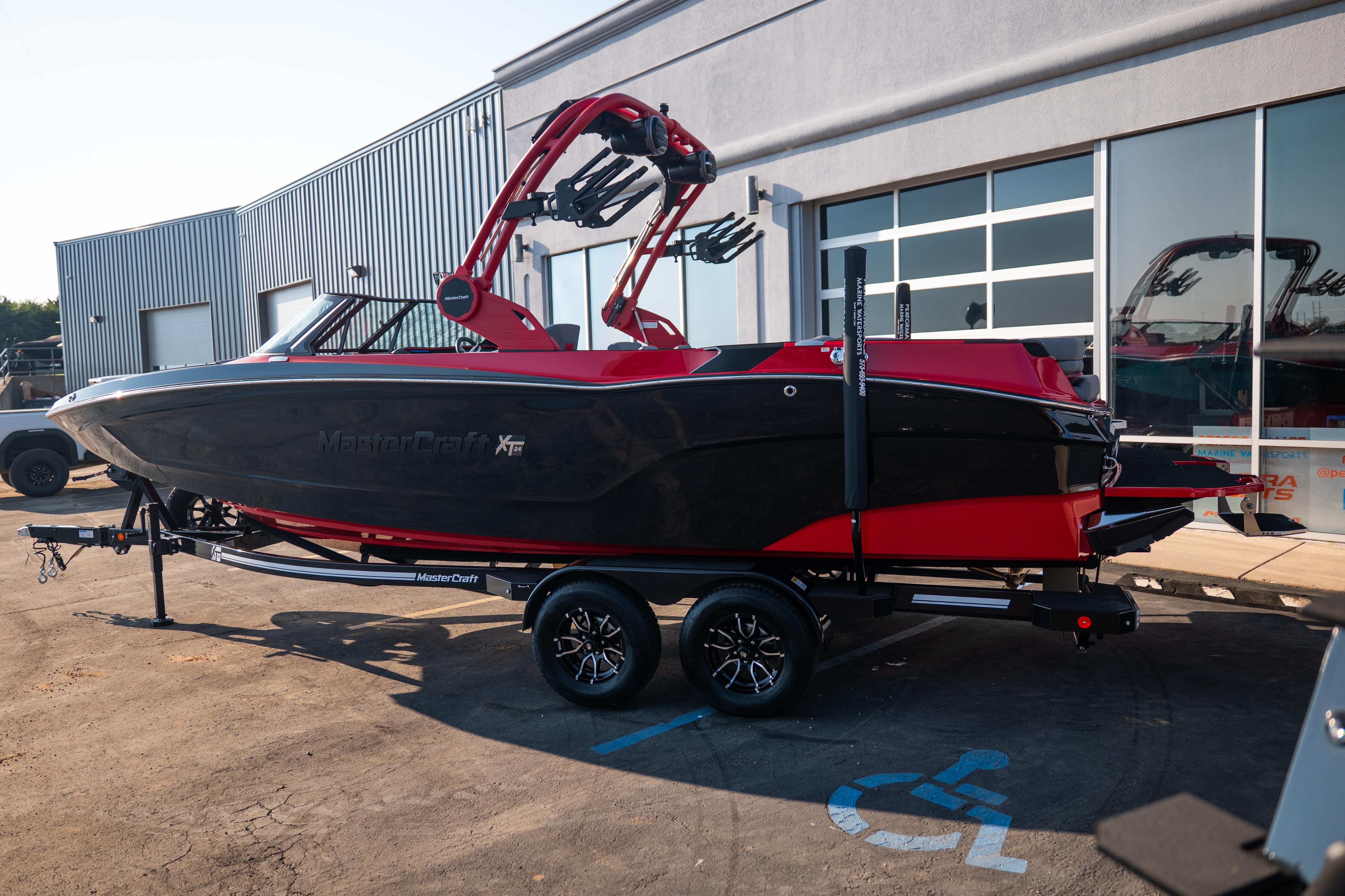 2027 MasterCraft XT24 boat in black and red on a trailer outside a building.