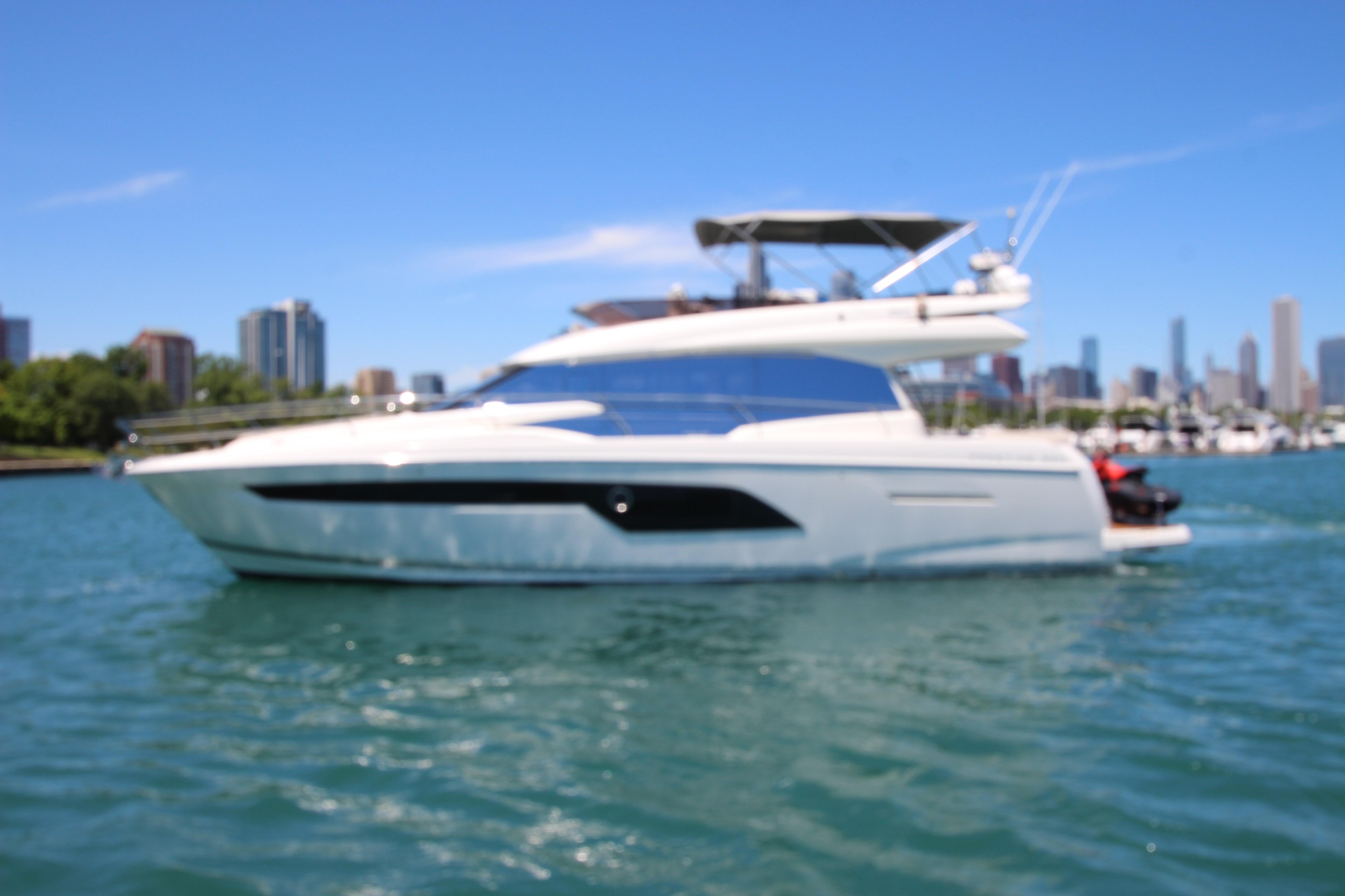 Luxury 2022 Prestige 520 yacht cruising on a sunny day with city skyline backdrop.