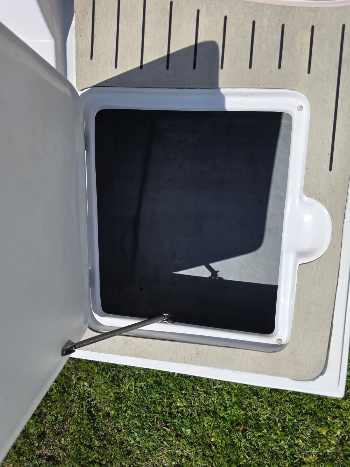 Open storage compartment on a boat with gray flooring and green grass in the background.