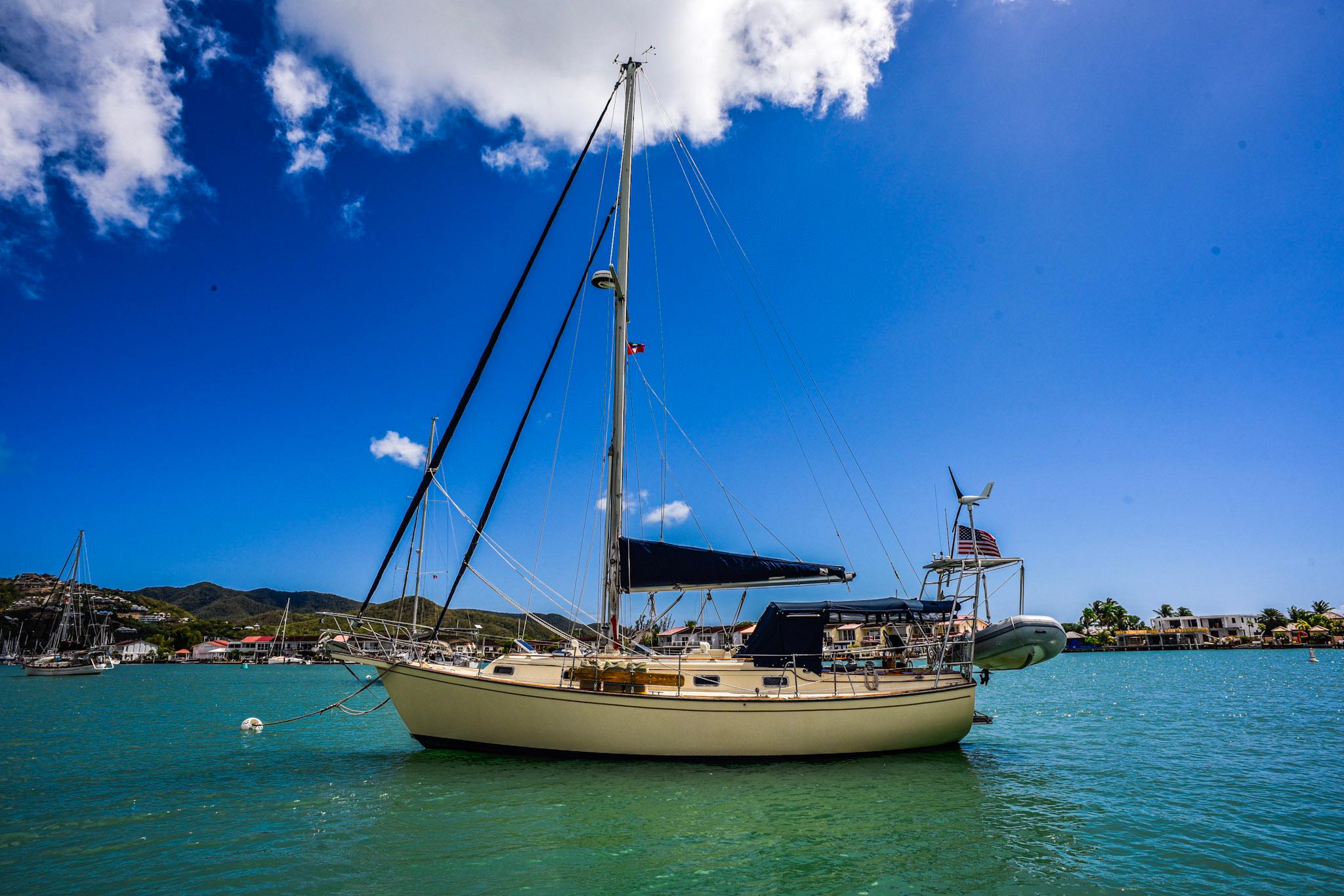 1989 Island Packet 35 Center Board sailboat anchored in a sunny, tropical harbor.