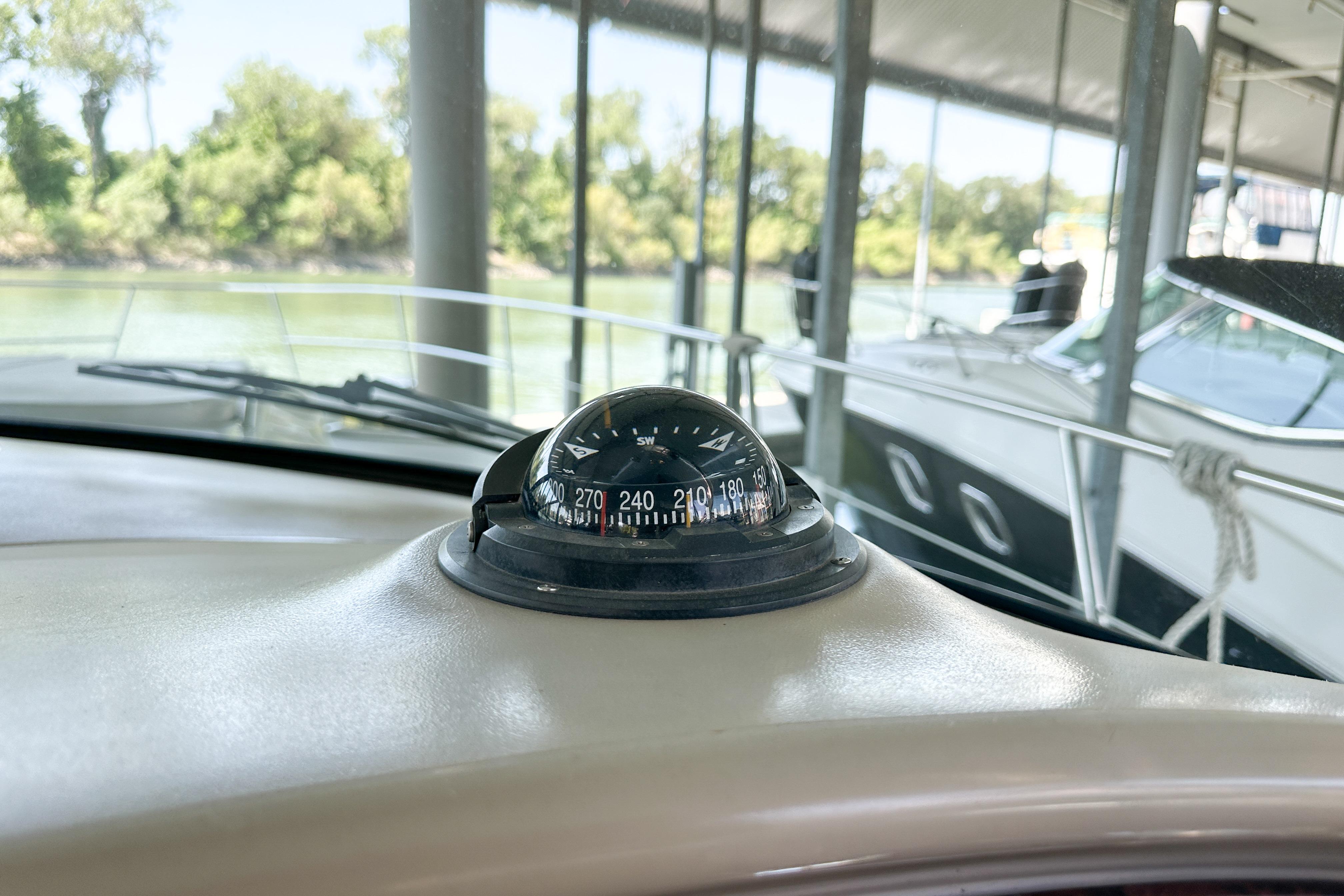 Compass on 2001 Sea Ray 410 Sundancer boat dashboard, docked near trees.