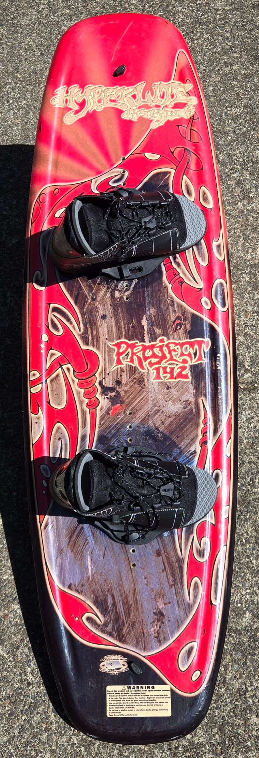 A red wakeboard with bold design and bindings on a concrete surface.
