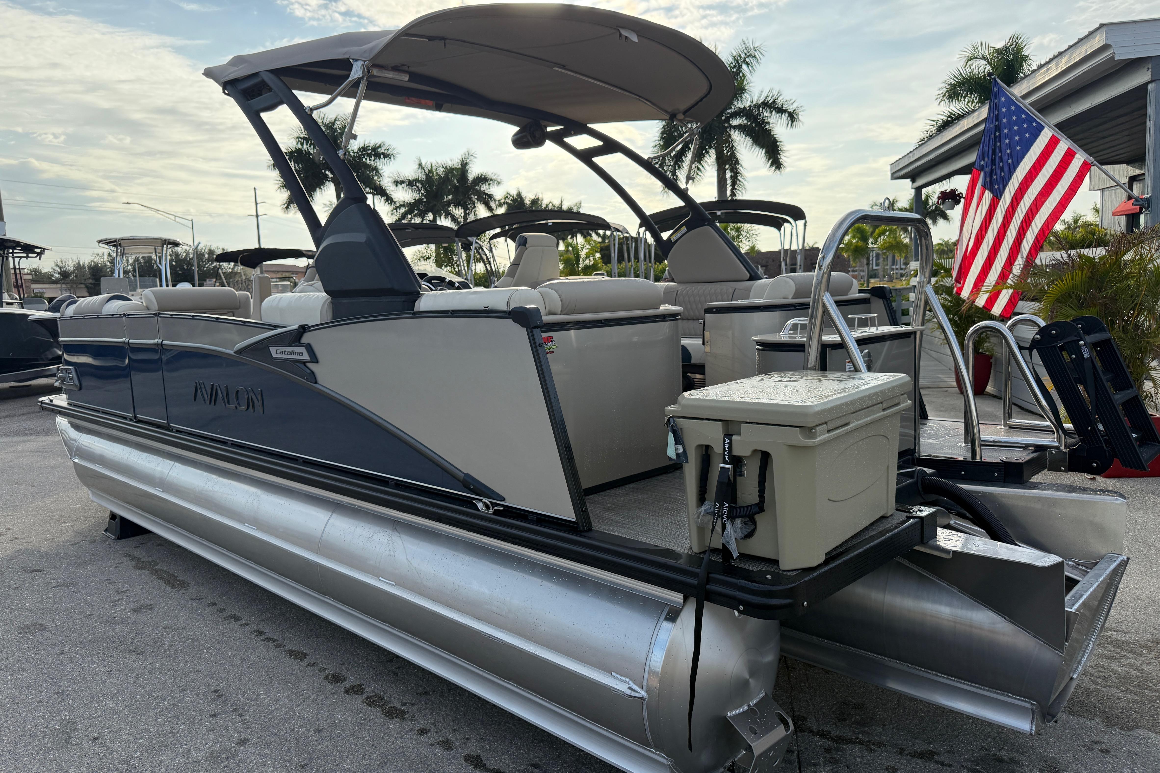 2026 Avalon 2385 Catalina Quad Lounger Tri Toon with American flag, parked outdoors.
