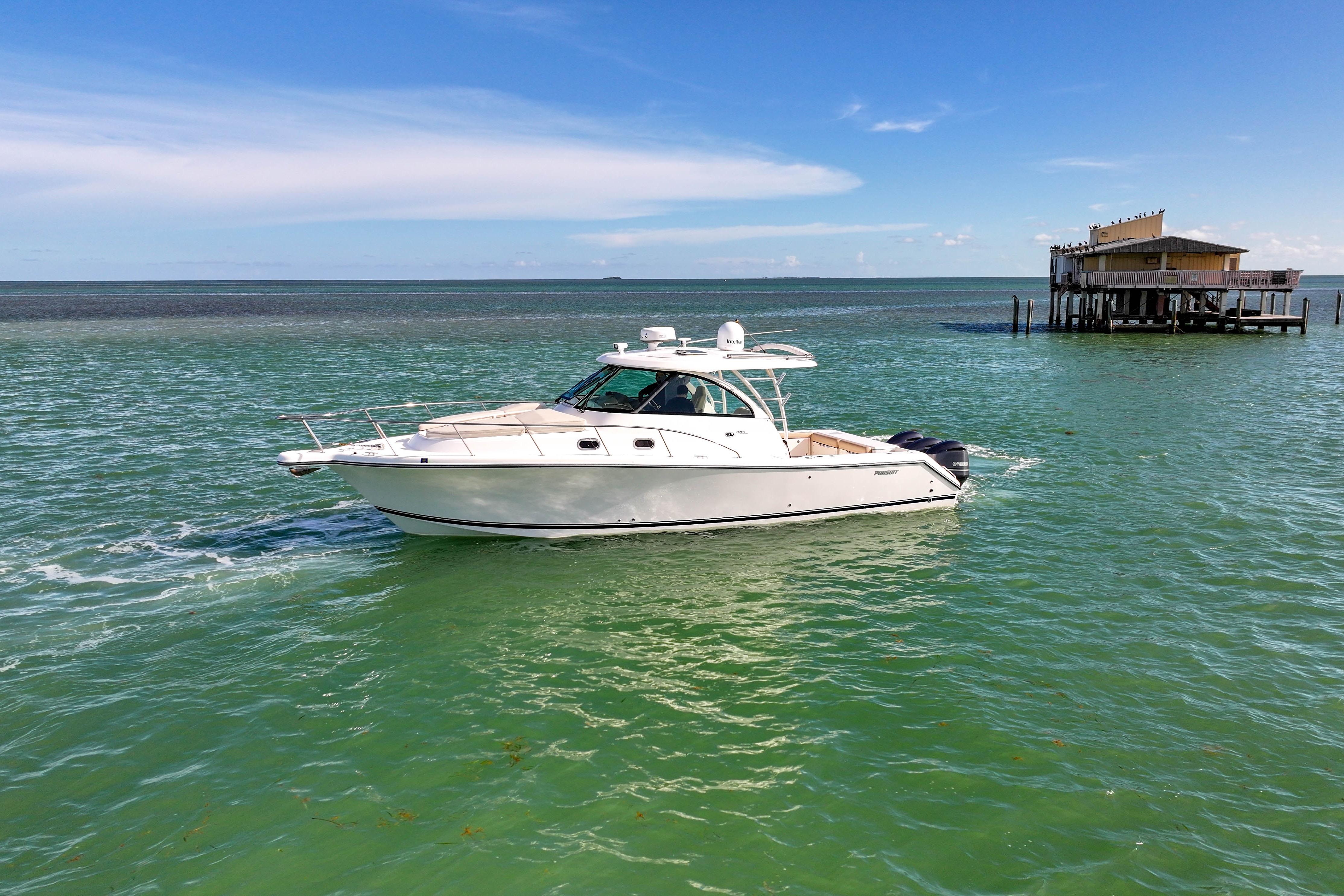2016 Pursuit OS 385 Offshore boat cruising on clear blue waters near a stilt house.