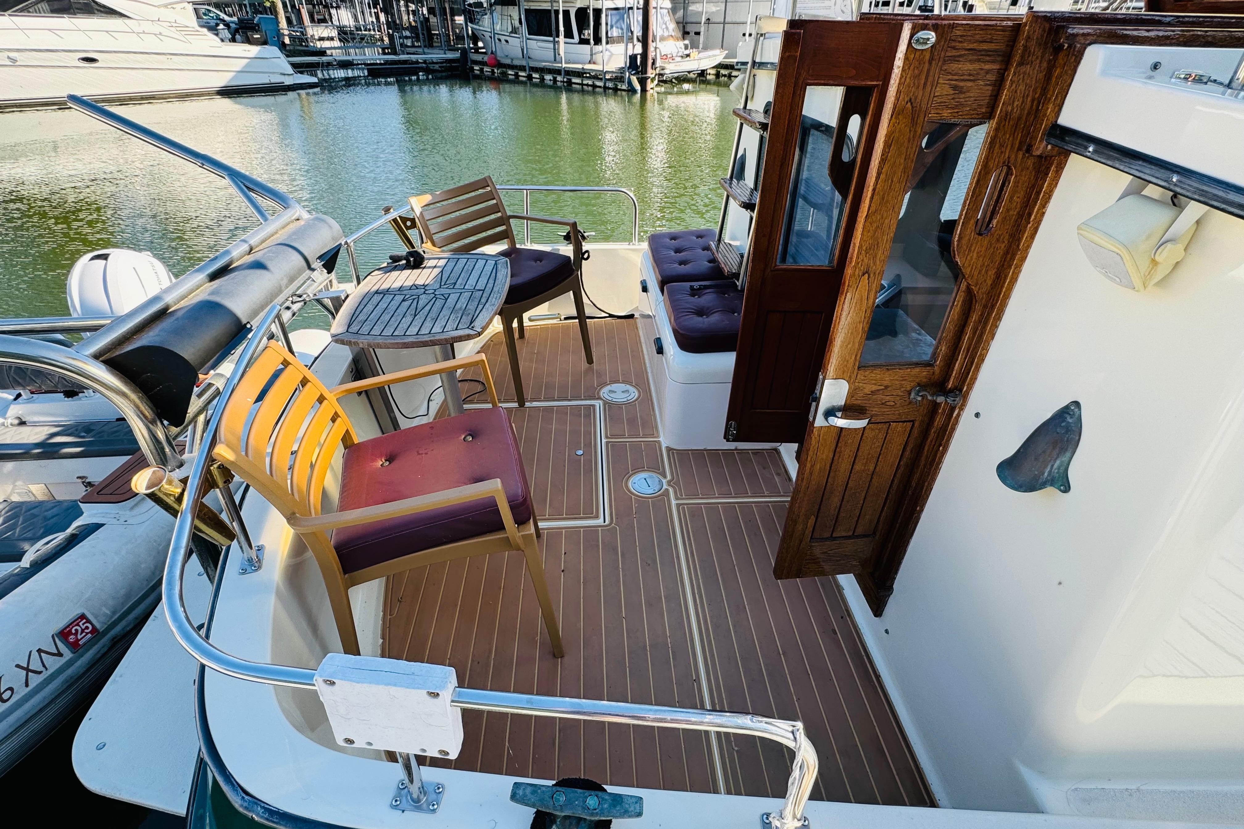 1996 Nordic Tug 32 boat deck with wooden chairs and table, docked at marina.