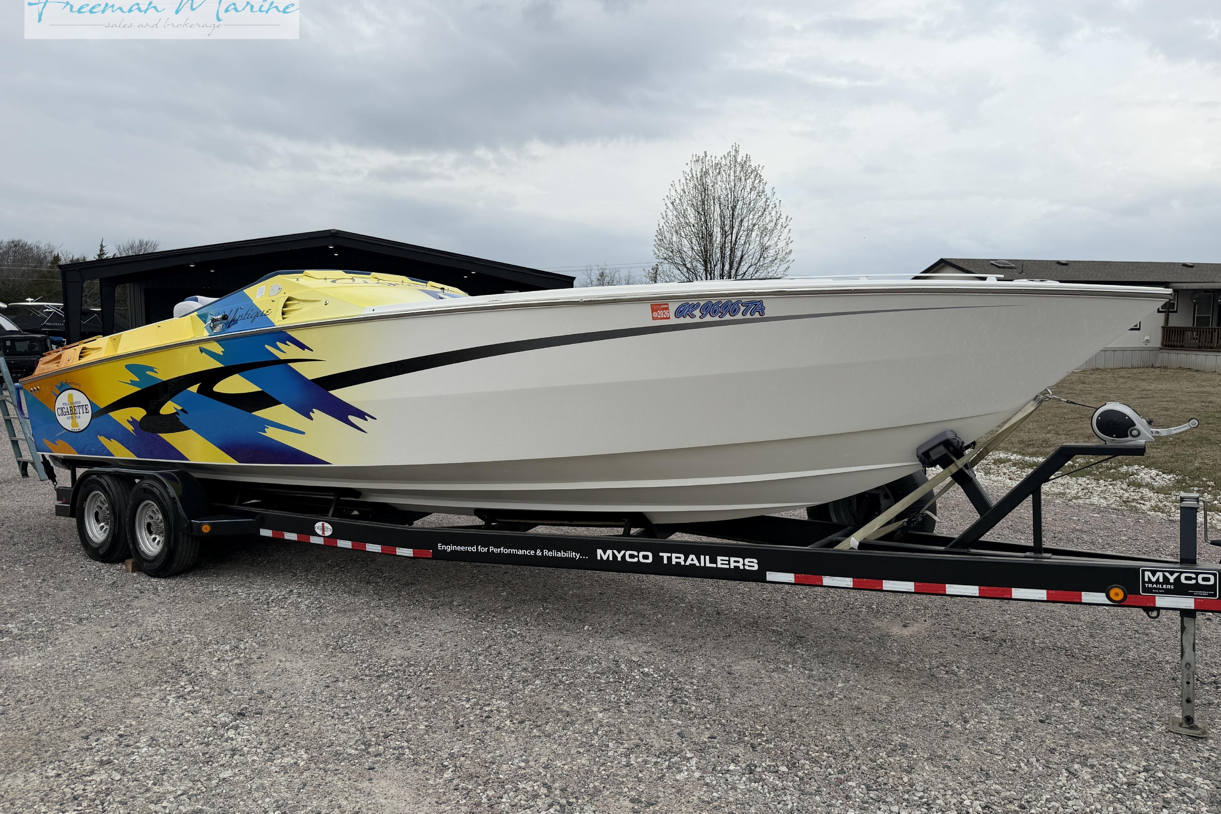2000 Cigarette 30' Mystique boat on trailer with colorful graphics, parked outdoors.
