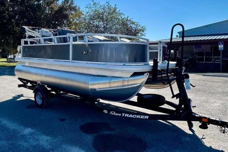 2026 Sun Tracker Bass Buggy 16 XL Select pontoon boat on trailer in parking lot.