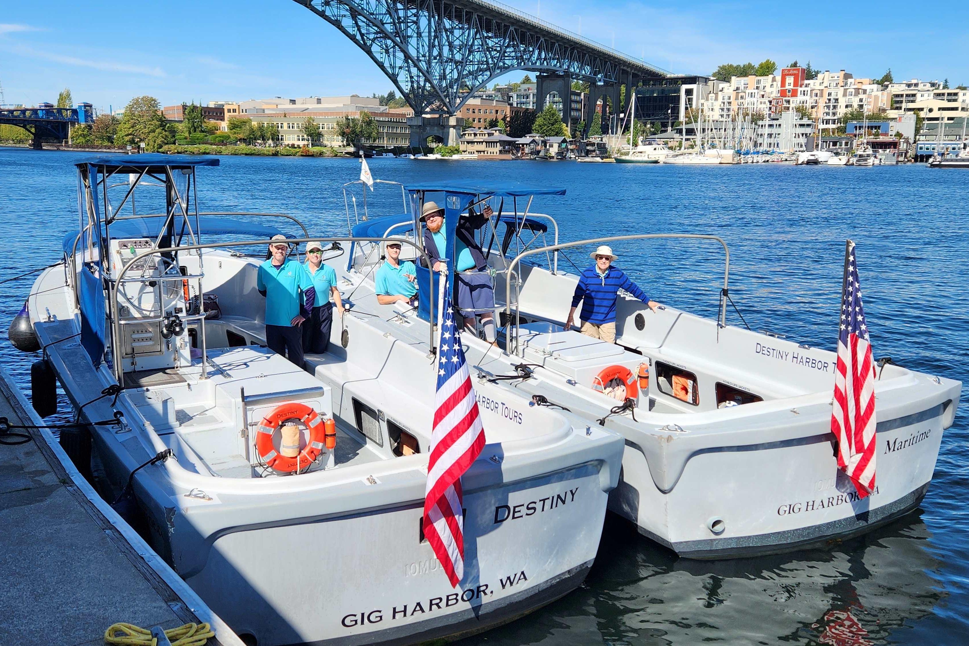 Two boats docked with crew, American flags, and a scenic waterfront backdrop.