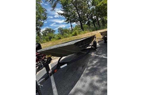 2025 Tracker Grizzly 1860 Utility boat on trailer, parked outdoors under trees.