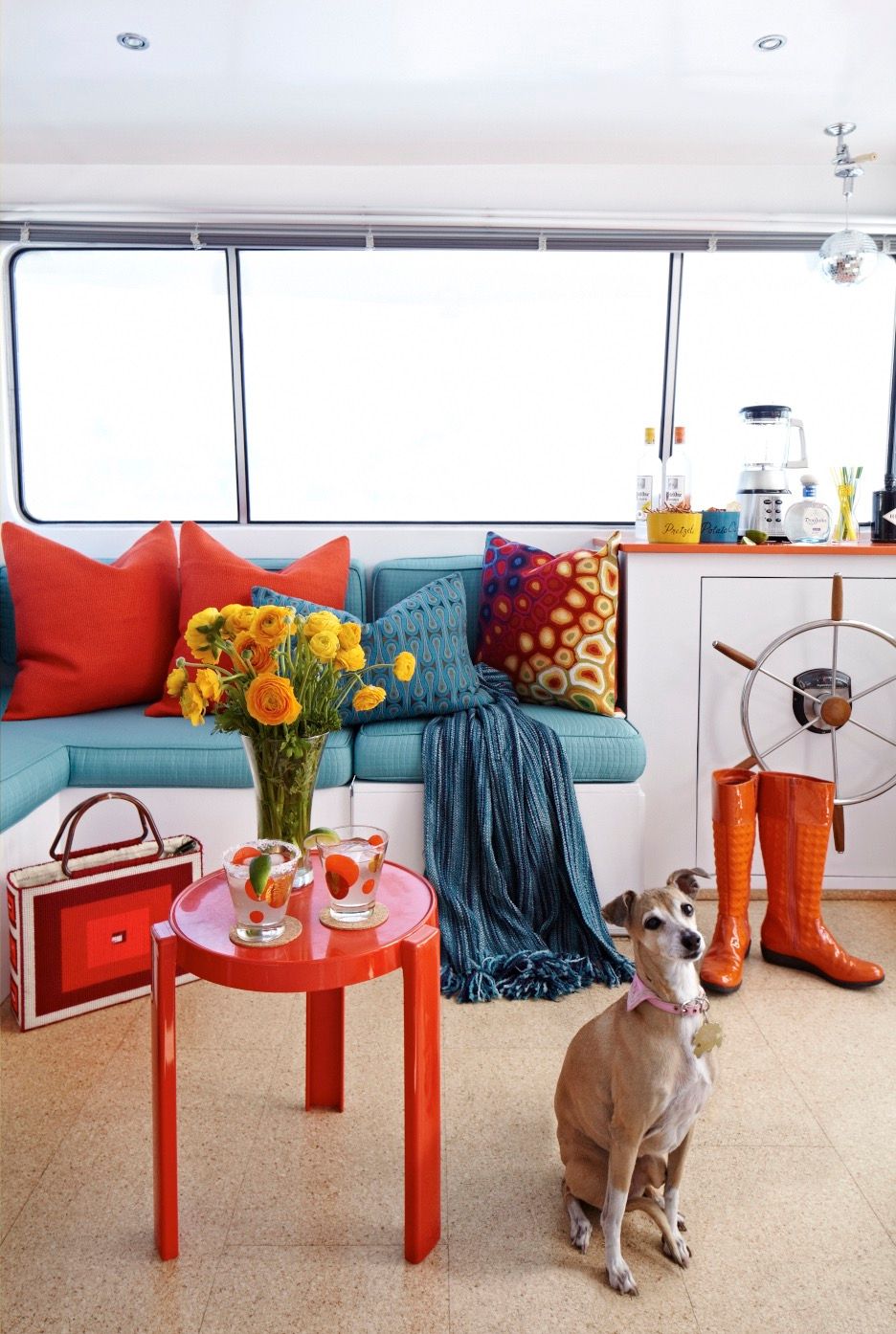 Interior of a houseboat with colorful decor, flowers, a dog, and a steering wheel.