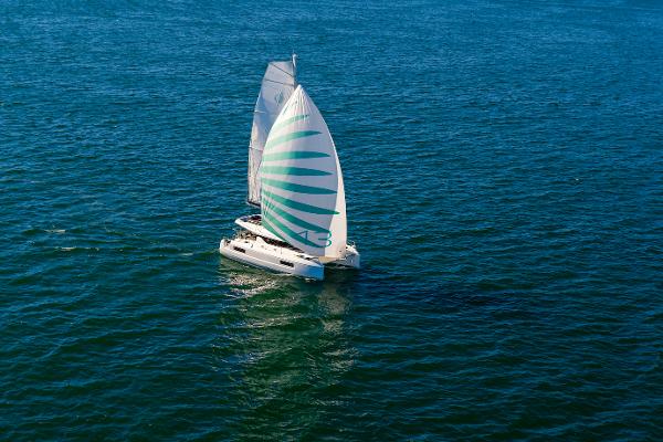 2025 Lagoon 43 catamaran sailing on open blue sea with striped sail.