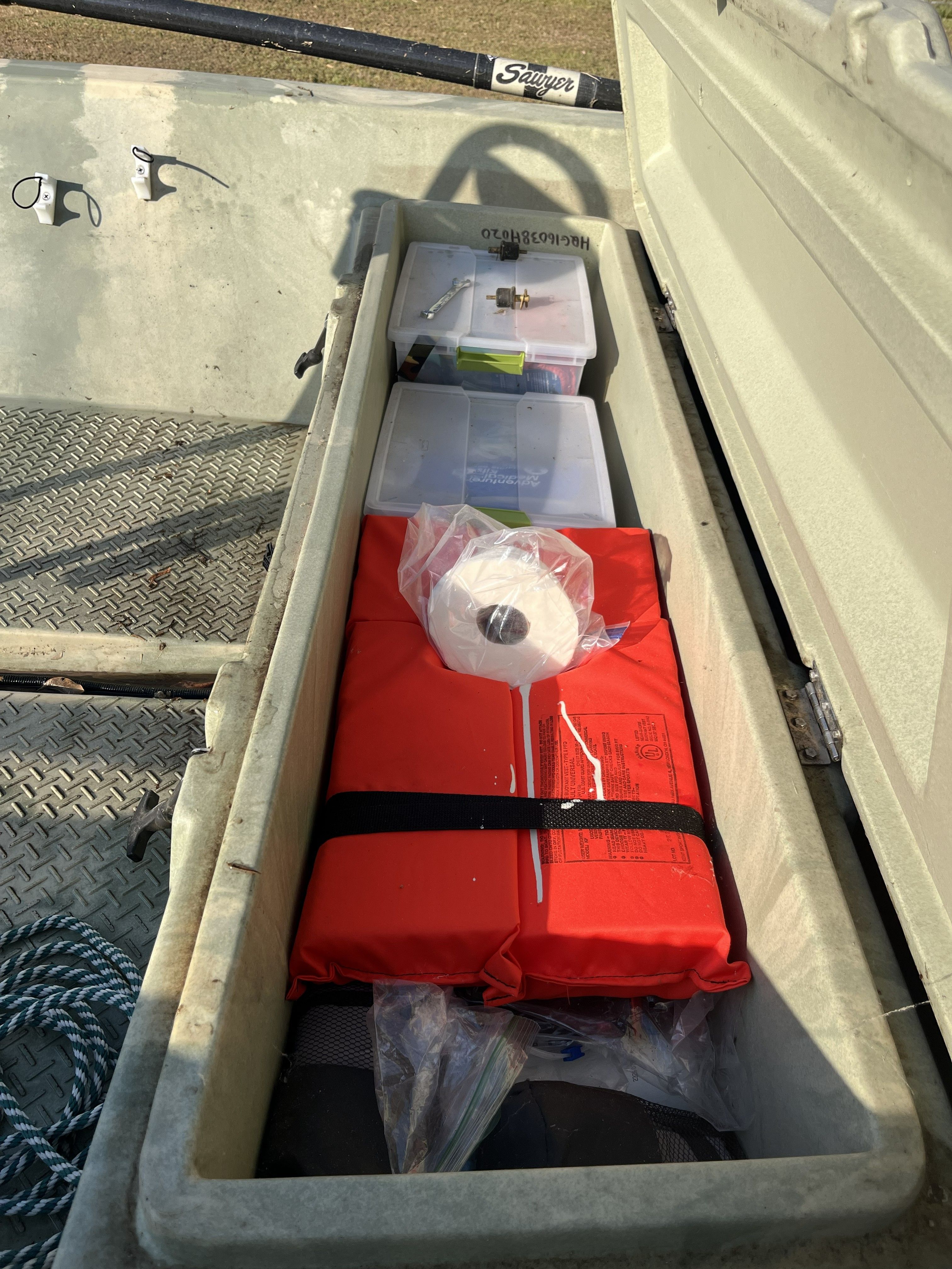 An open storage compartment in a boat with a life jacket, rope, and fishing gear.