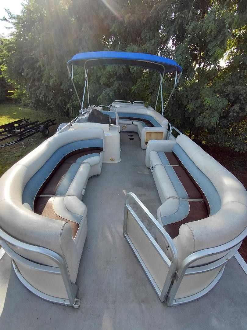 A 1999 Premier 250 Grand Majestic pontoon boat with blue and white seating and a blue canopy.