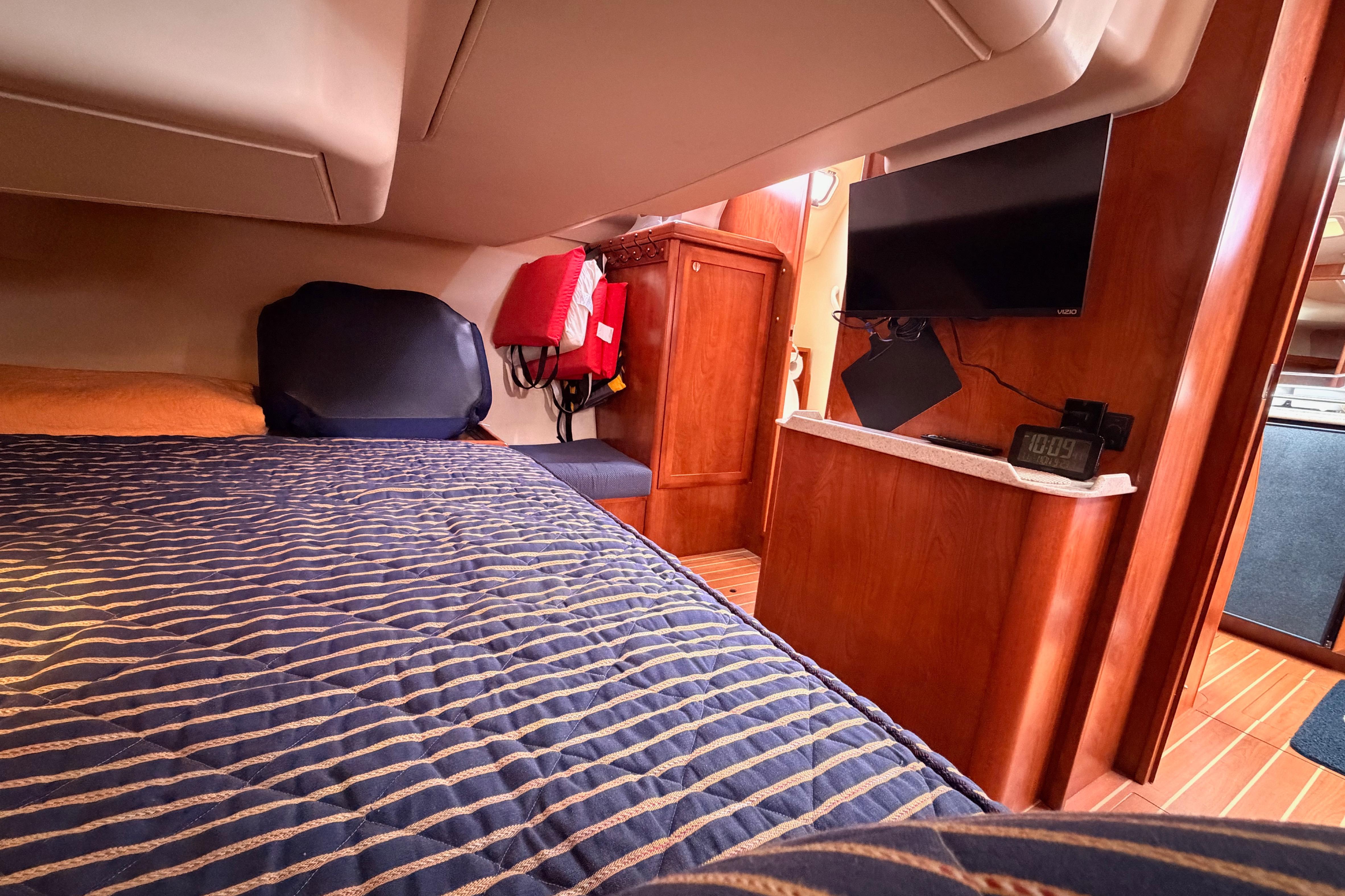 Cozy cabin interior of 2009 Hunter 38 yacht with bed, TV, and wooden furnishings.