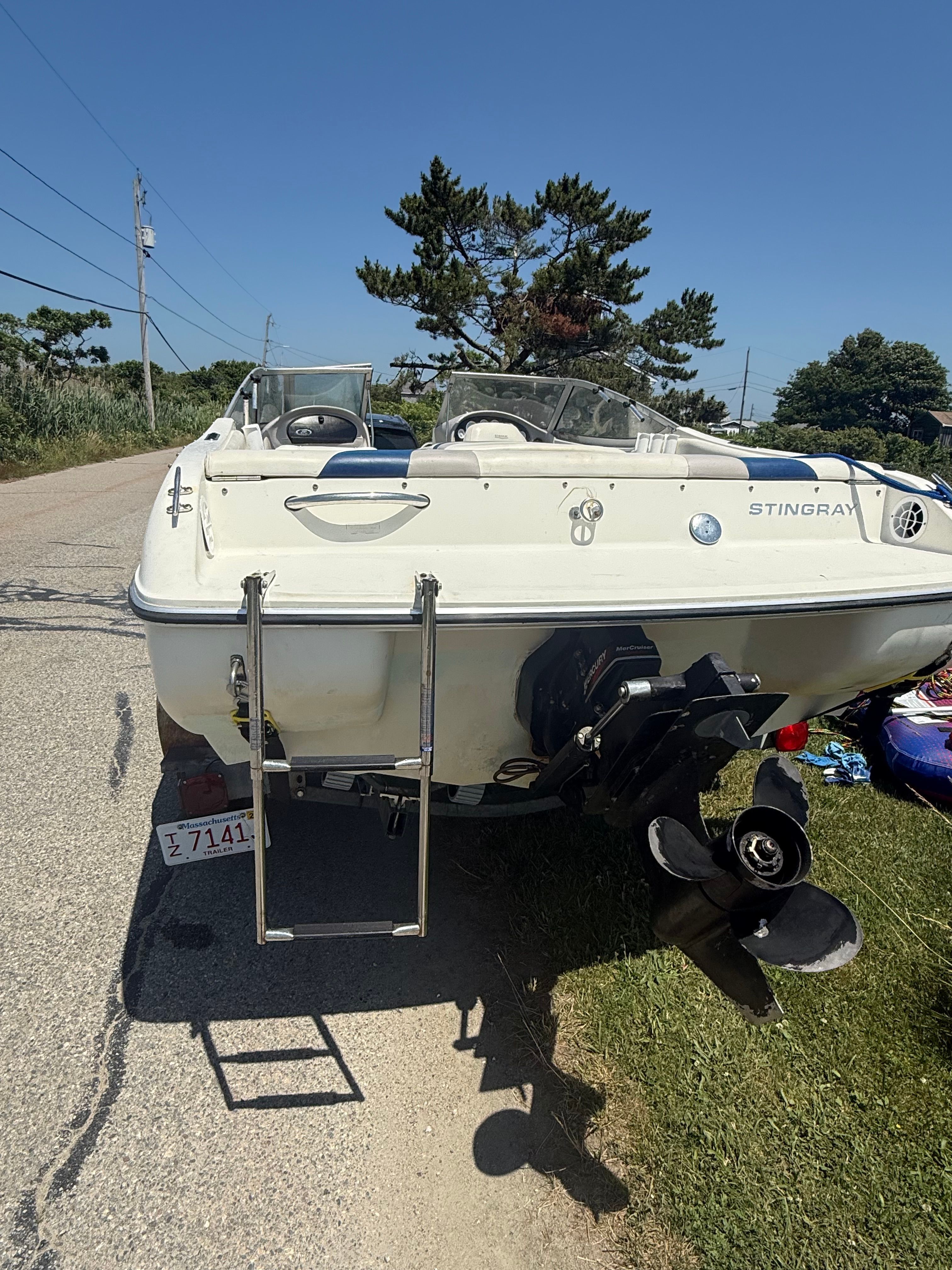 A white motorboat on a trailer on land, featuring an outboard motor and a ladder.