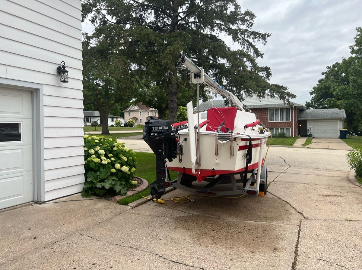 A boat on a trailer in a driveway, surrounded by houses and trees.