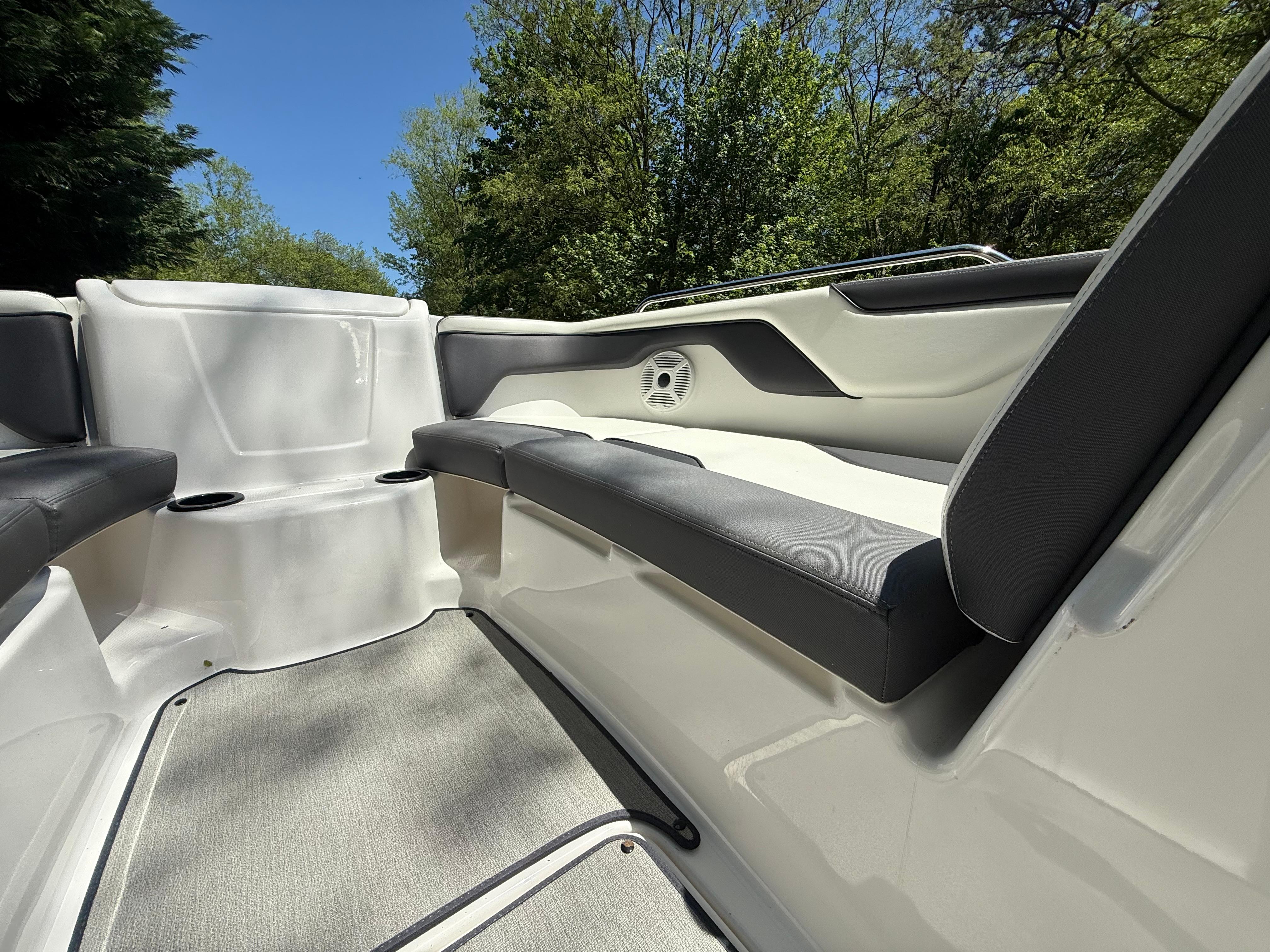 2022 Yamaha AR210 boat interior with cushioned seating and speaker, surrounded by trees.