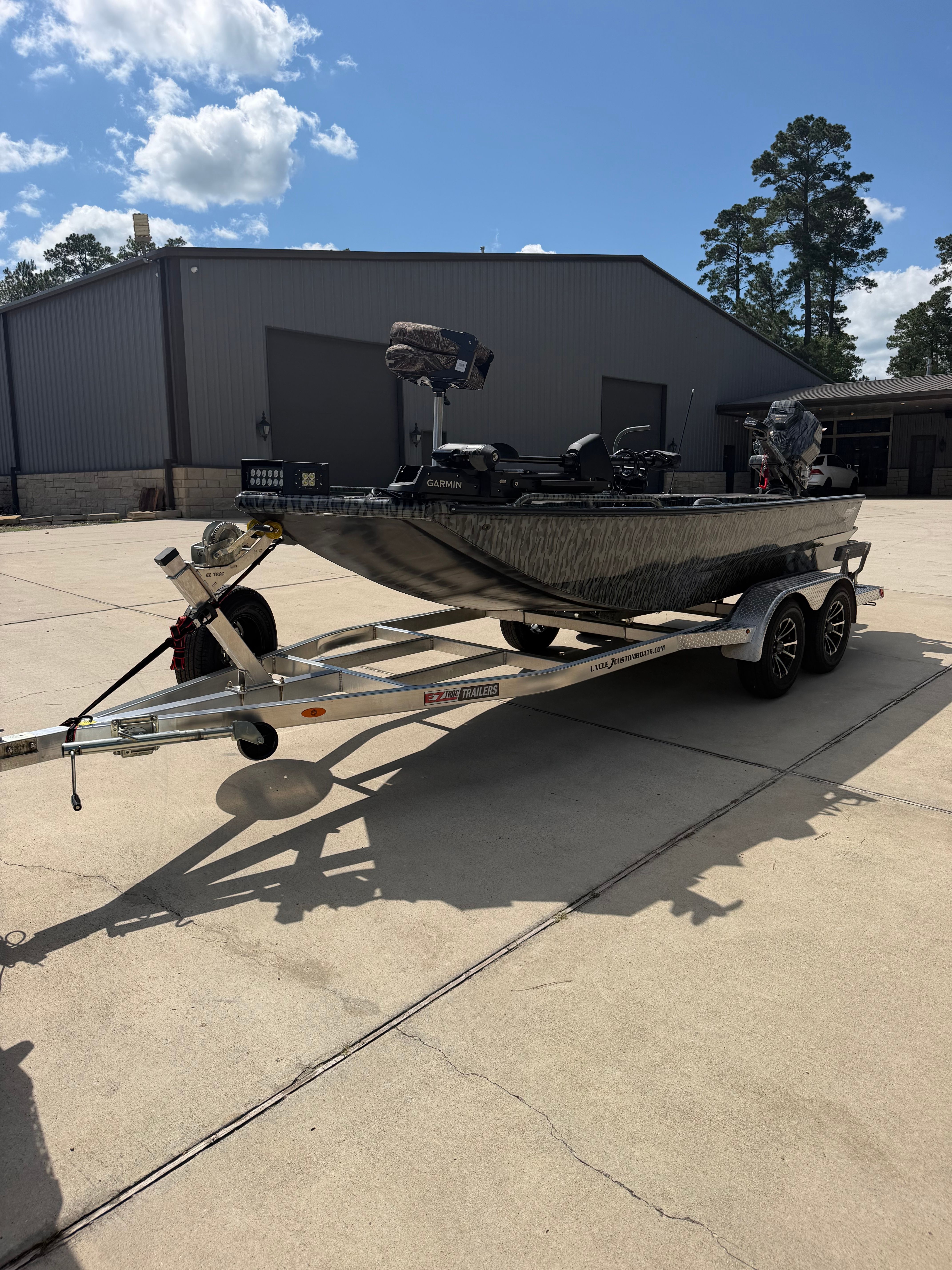 A gray boat on a trailer is parked on a concrete lot in front of a building.