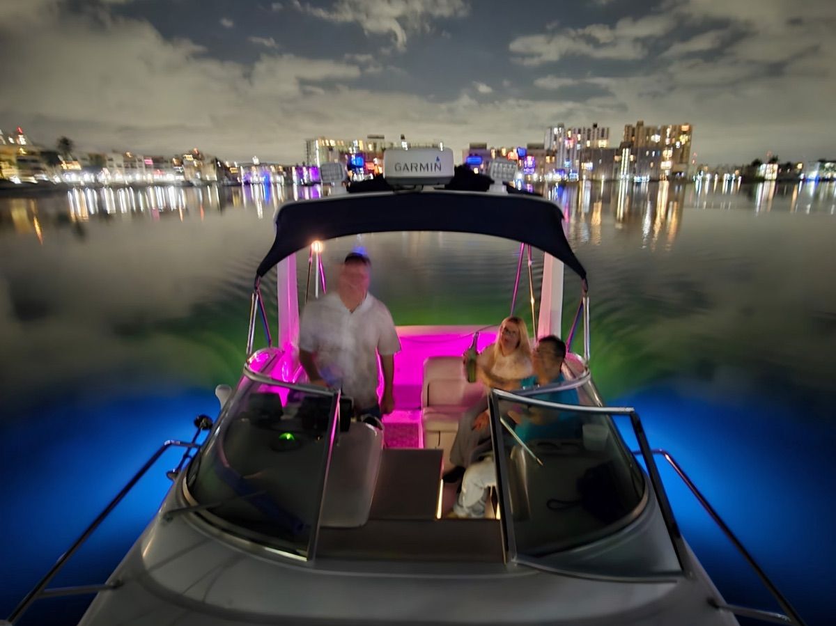 A Sea Ray Sundancer 260 boat with colorful lighting on calm water at night.