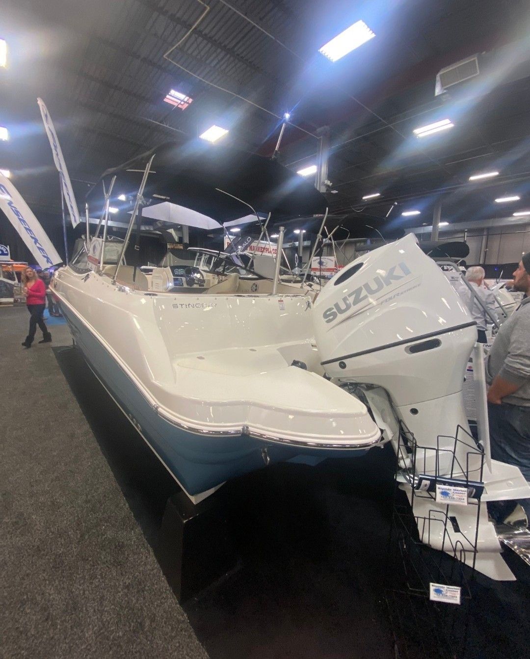A white boat with a Suzuki engine is displayed in an exhibition hall.