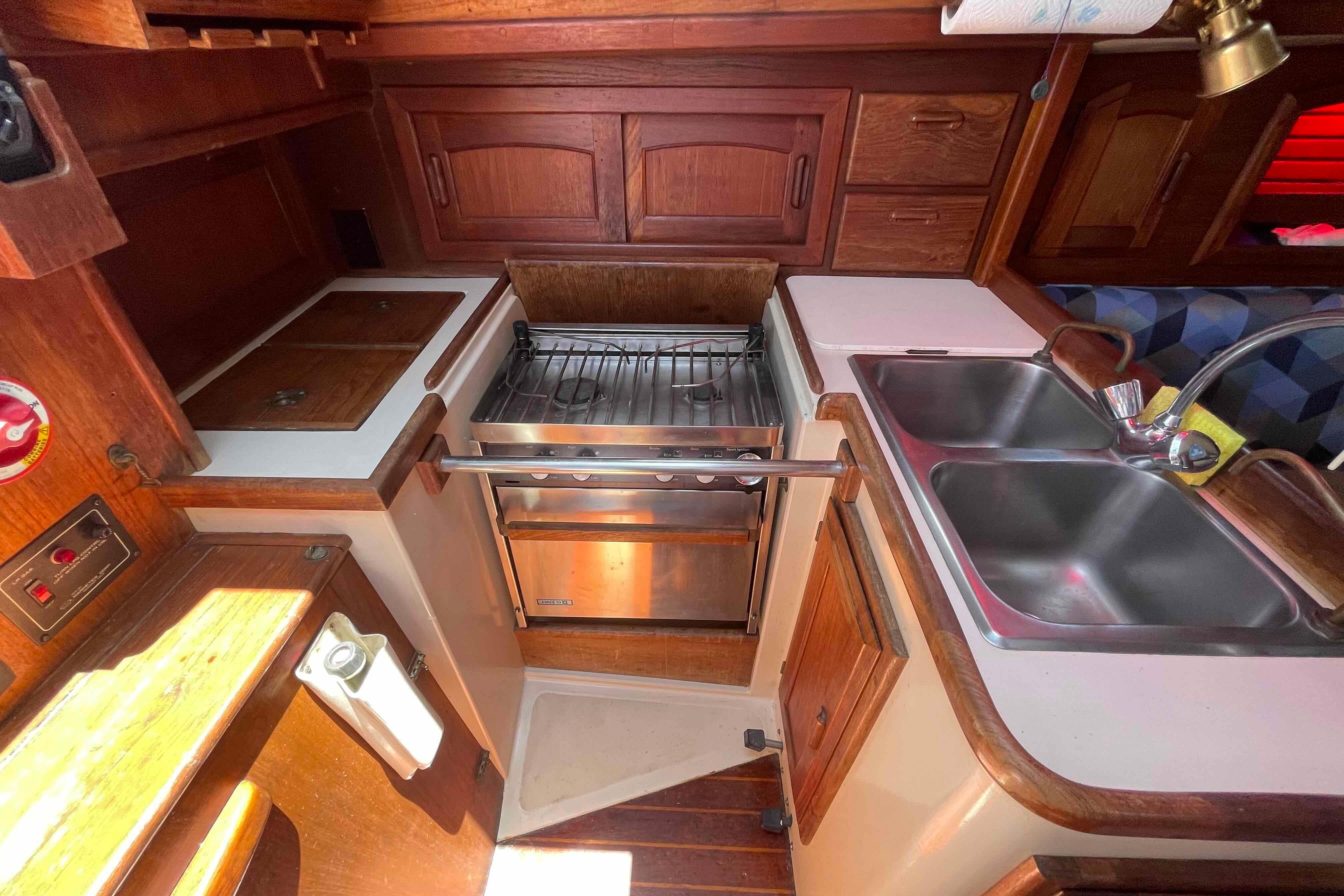 Cozy 1987 Pacific Seacraft 34 yacht kitchen with stove, sink, and wooden cabinetry.