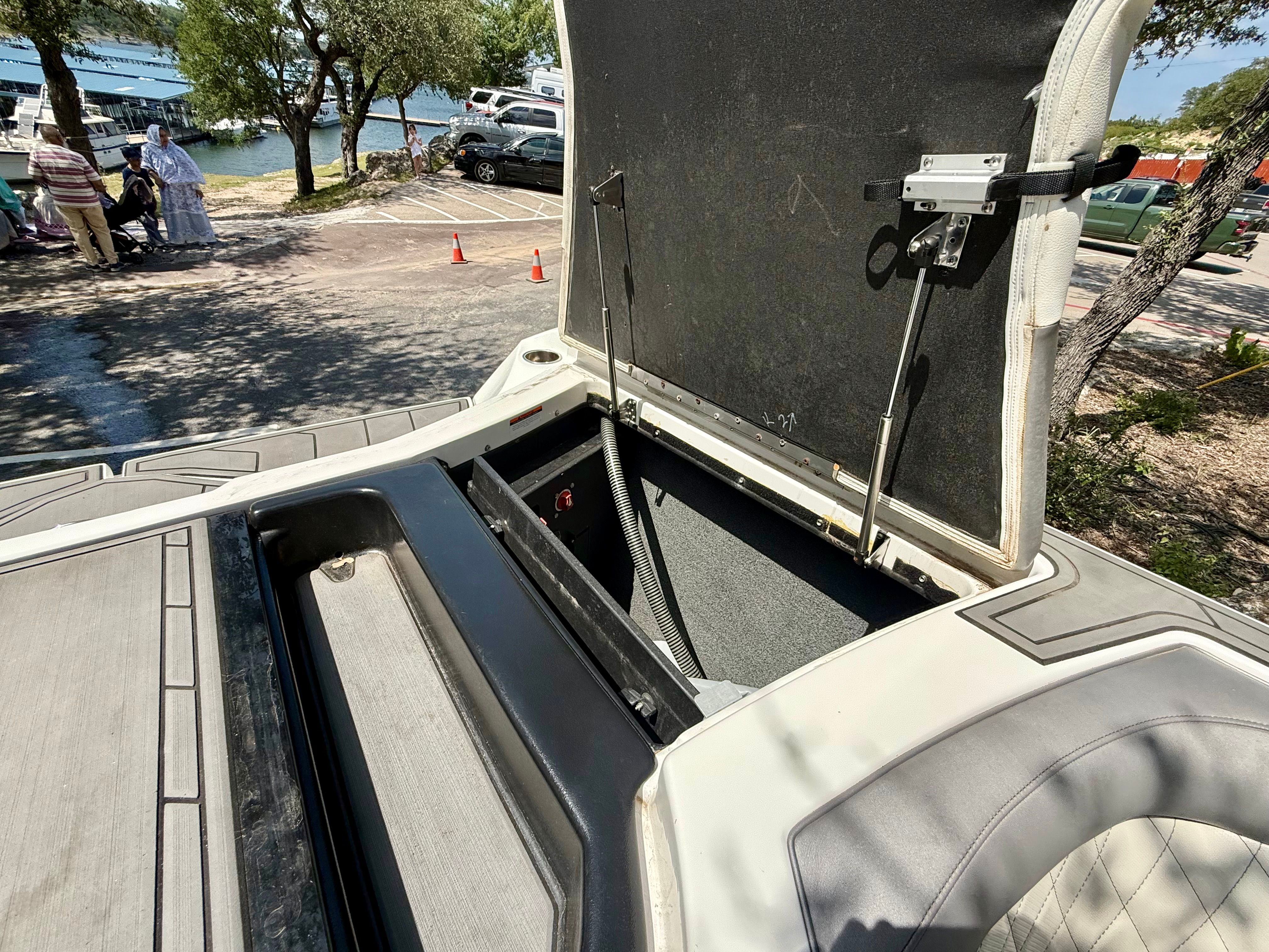An open storage compartment on a boat with a view of a parking lot and trees.
