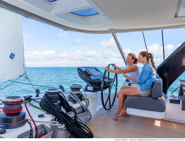 Two people sailing on a 2025 Lagoon SIXTY 5 catamaran, enjoying the open sea.