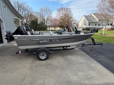 A silver Crestliner boat on a trailer, parked on a driveway next to a house.