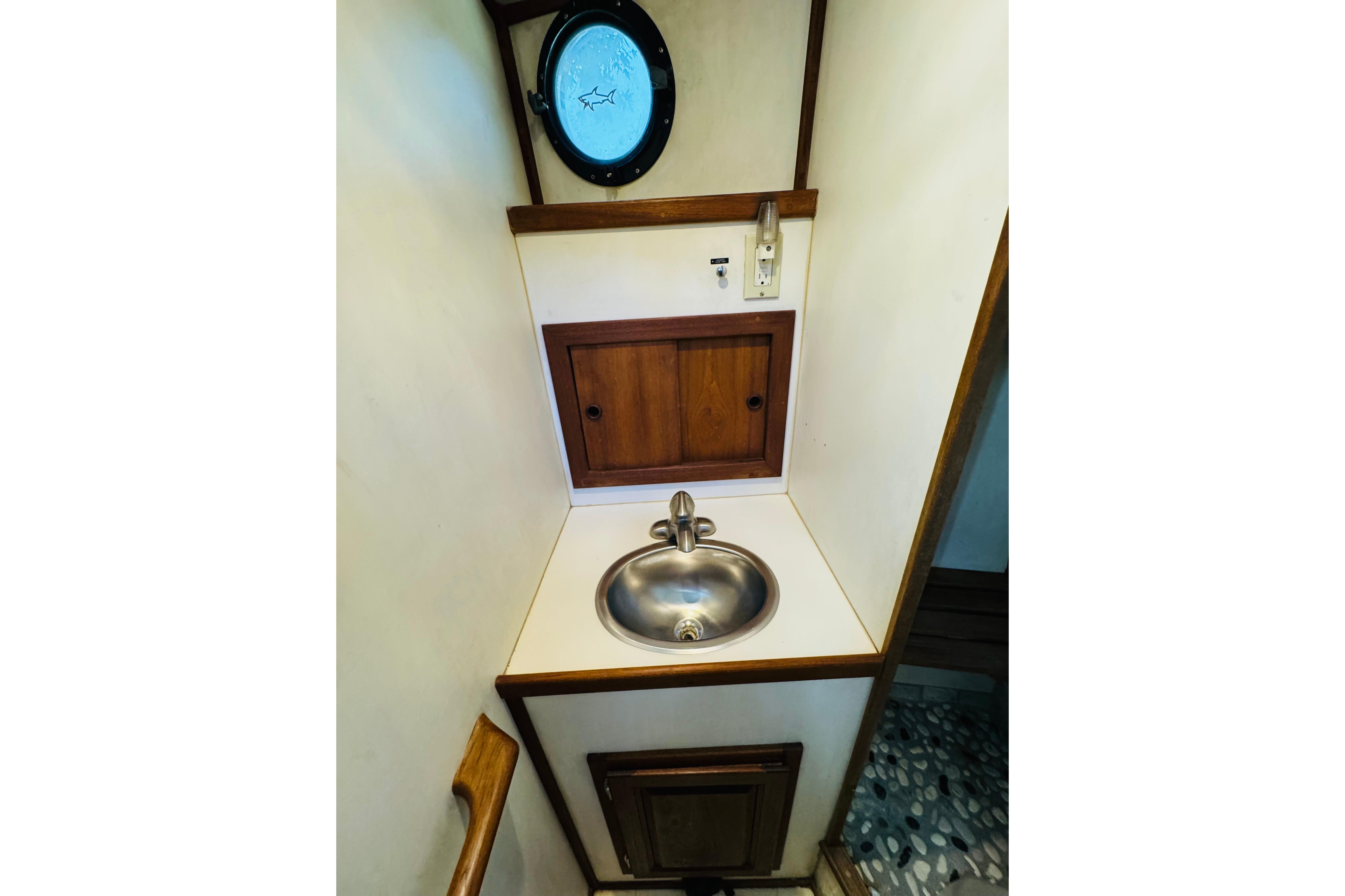 Compact bathroom sink area in a 1996 Nordic Tug 32 boat, featuring a porthole window.