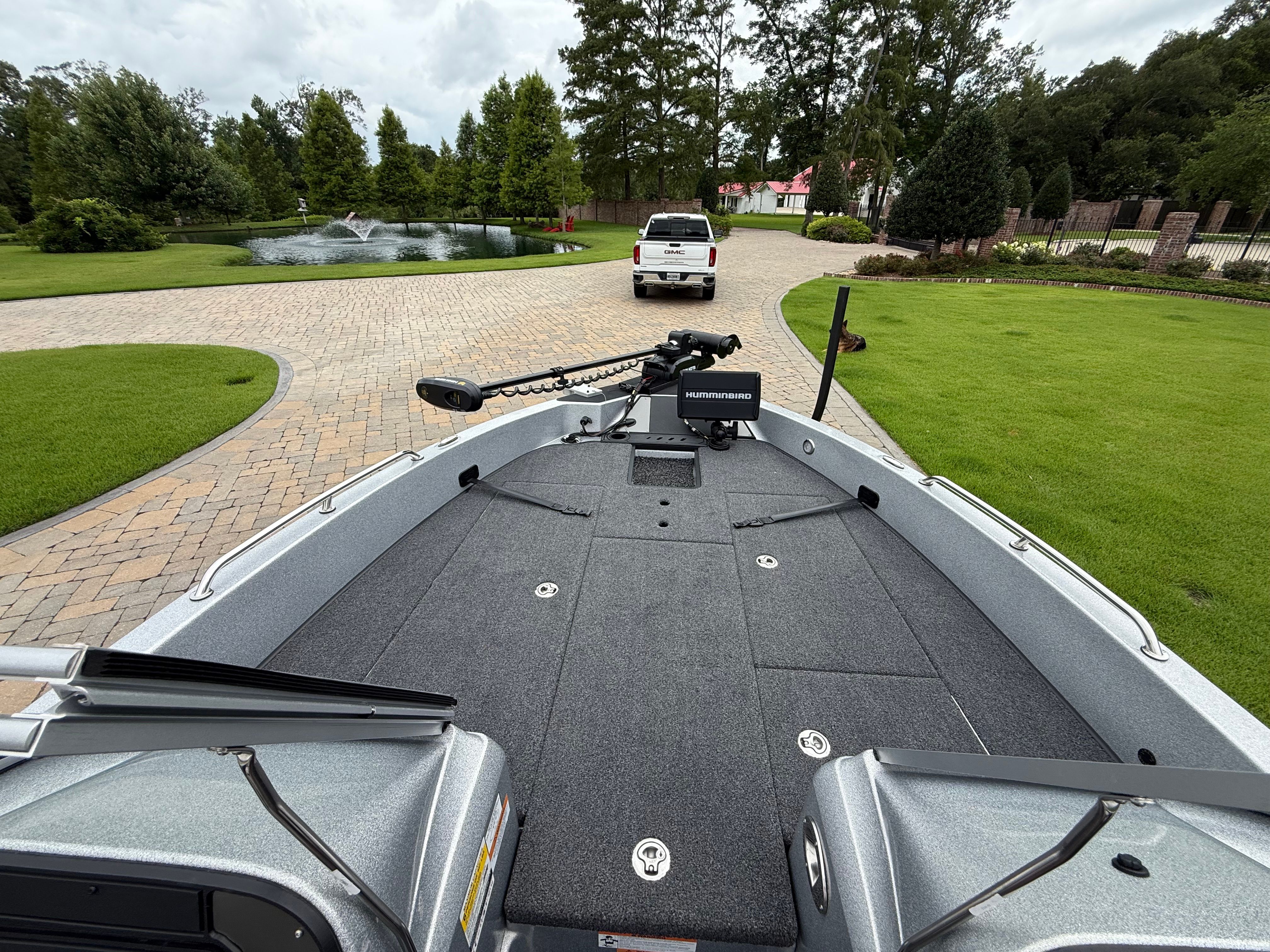 The image shows the deck of a Triton 206 Allure boat on a trailer, with a park-like background.