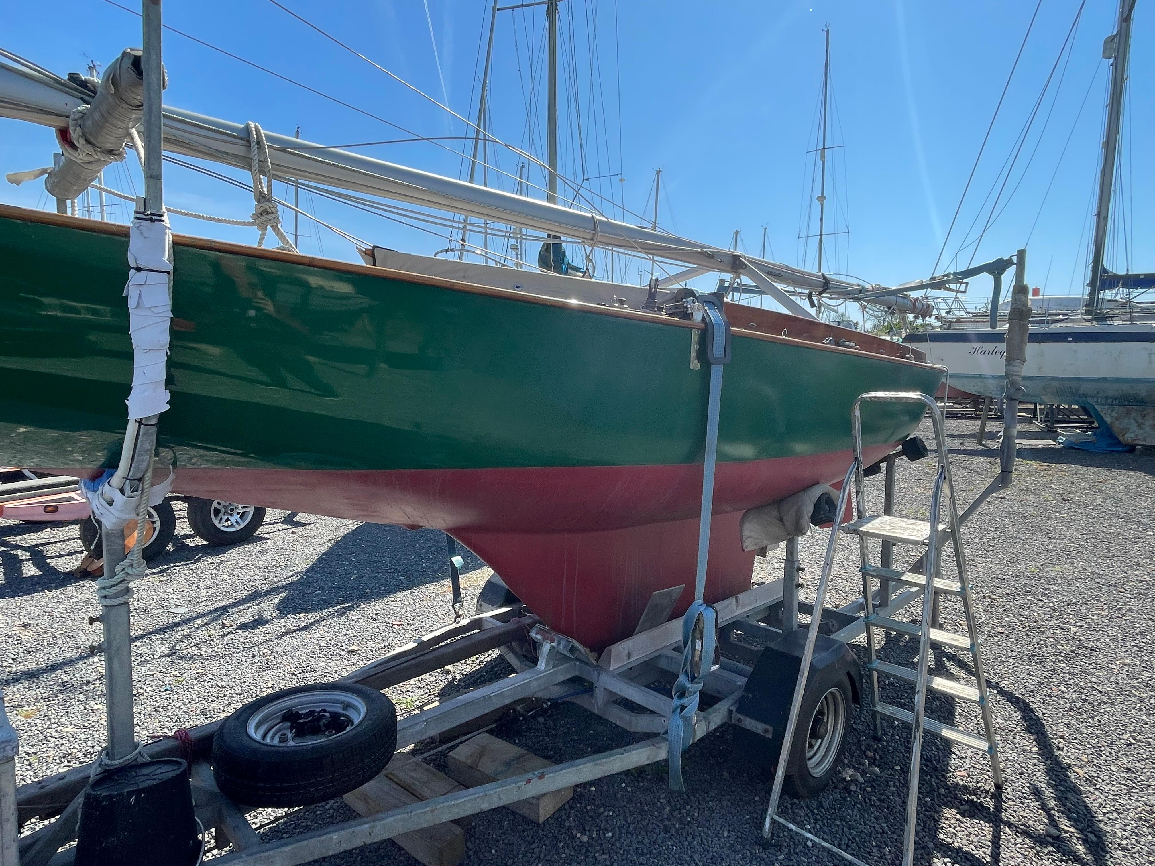 Green and red 2010 One Design Safe Harbour 12 sailboat on trailer in a boatyard.