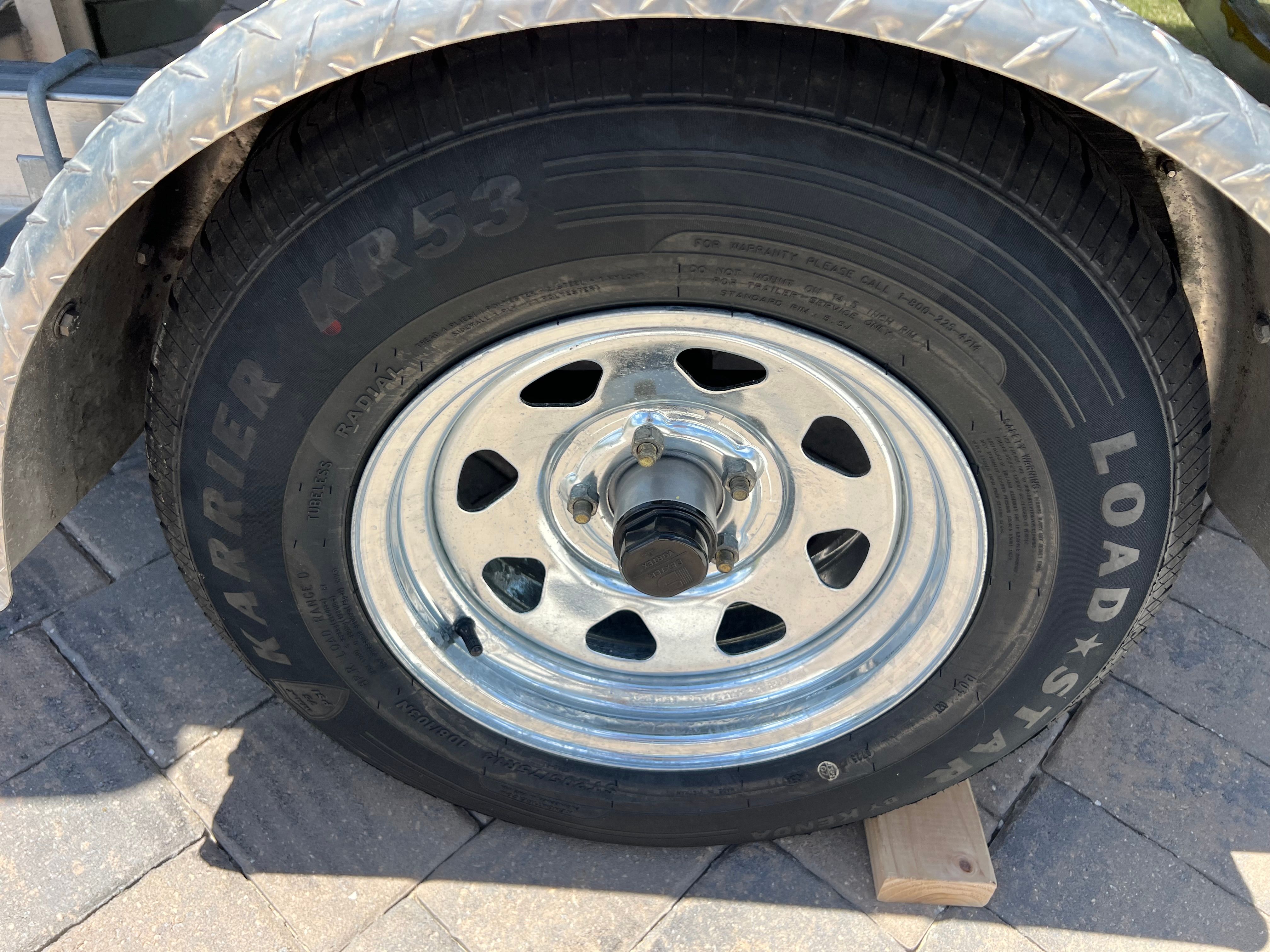 A shiny wheel of a boat trailer sits on a paved surface.