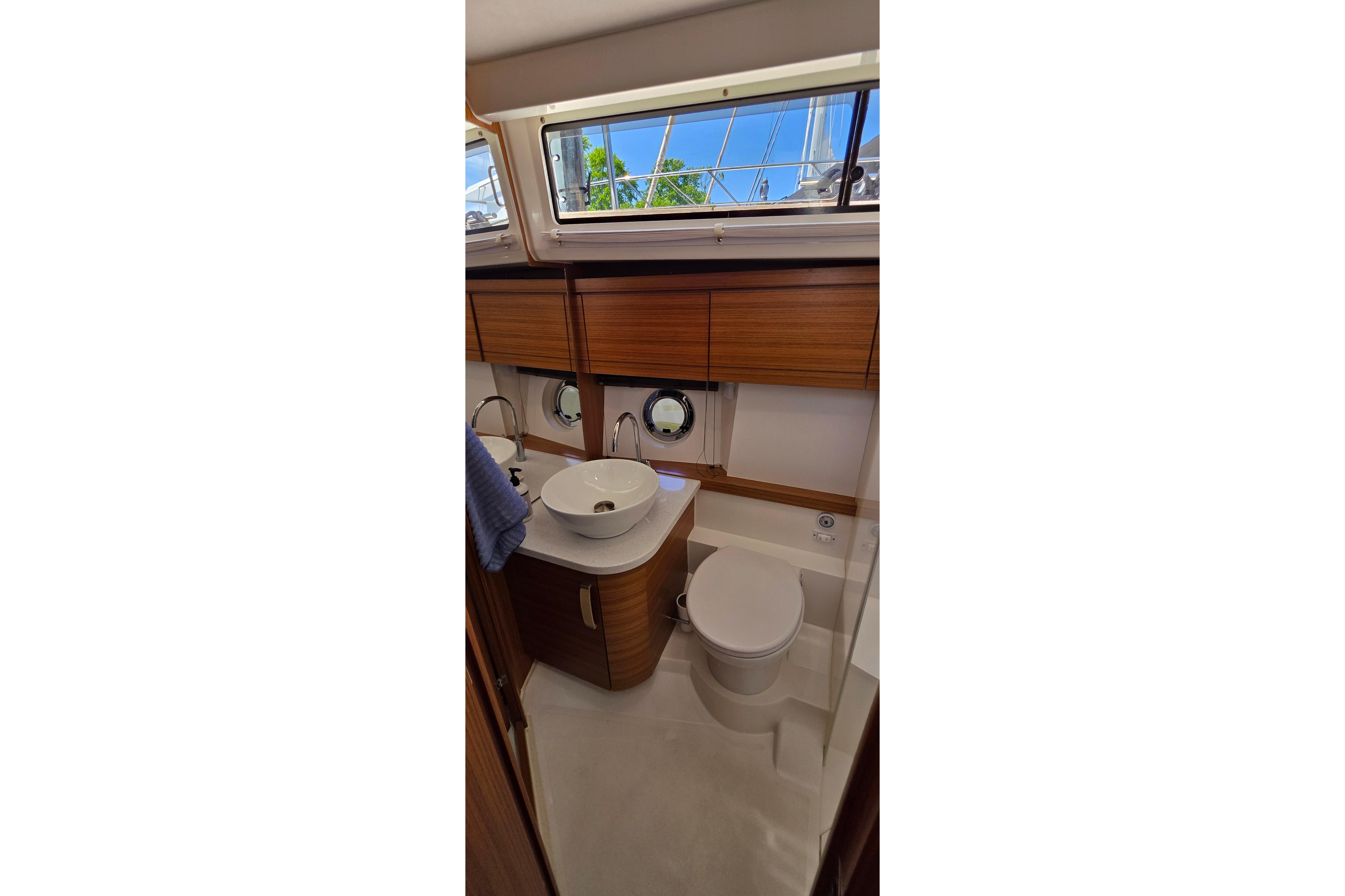 Modern bathroom interior of 2023 Greenline 40 yacht with wooden cabinetry and porthole windows.