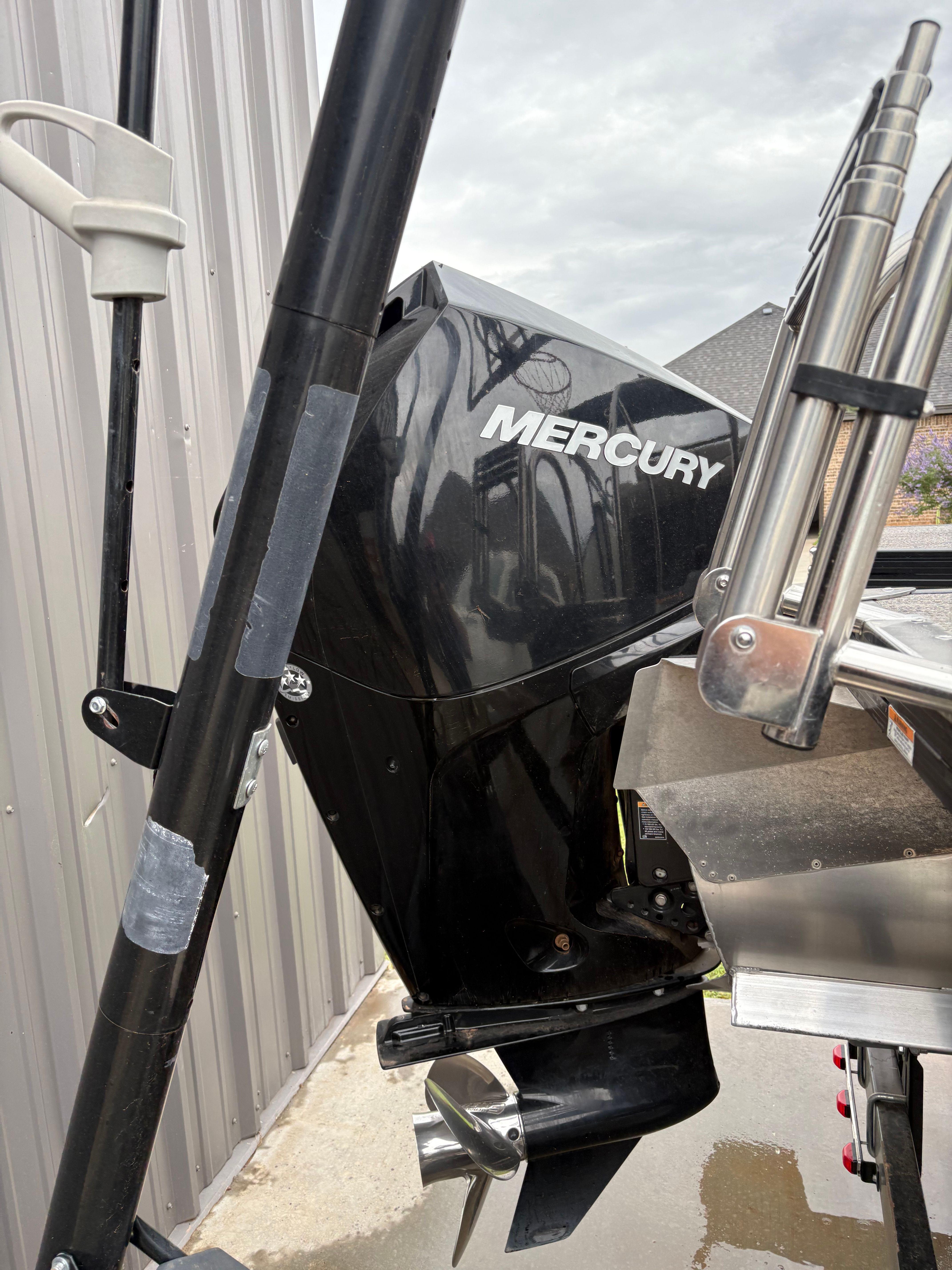 A Mercury outboard motor on a boat, next to a metal ladder and a building.