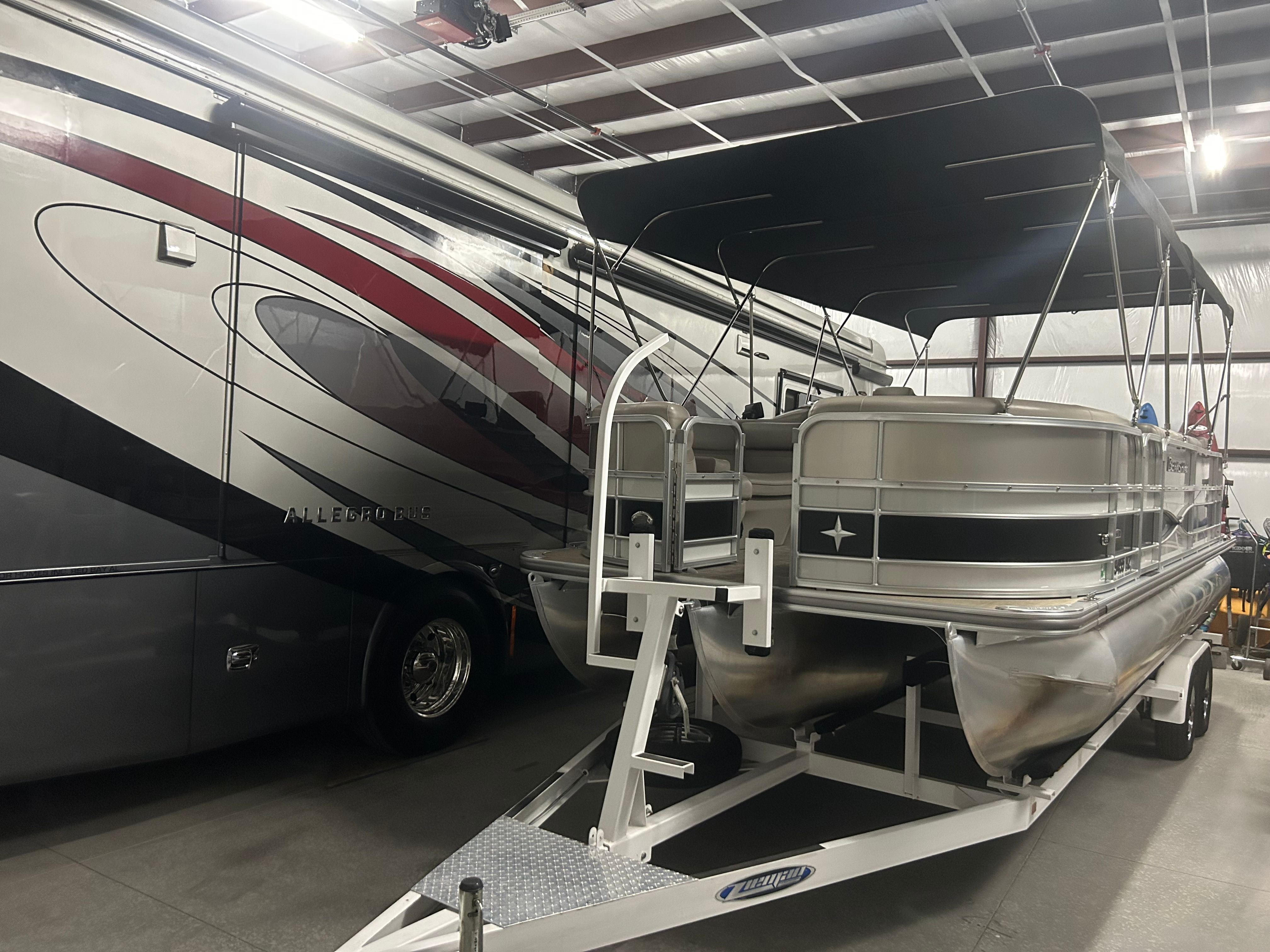 A 2018 Berkshire 24RFX CTS pontoon boat is on a trailer in a warehouse next to a large RV.