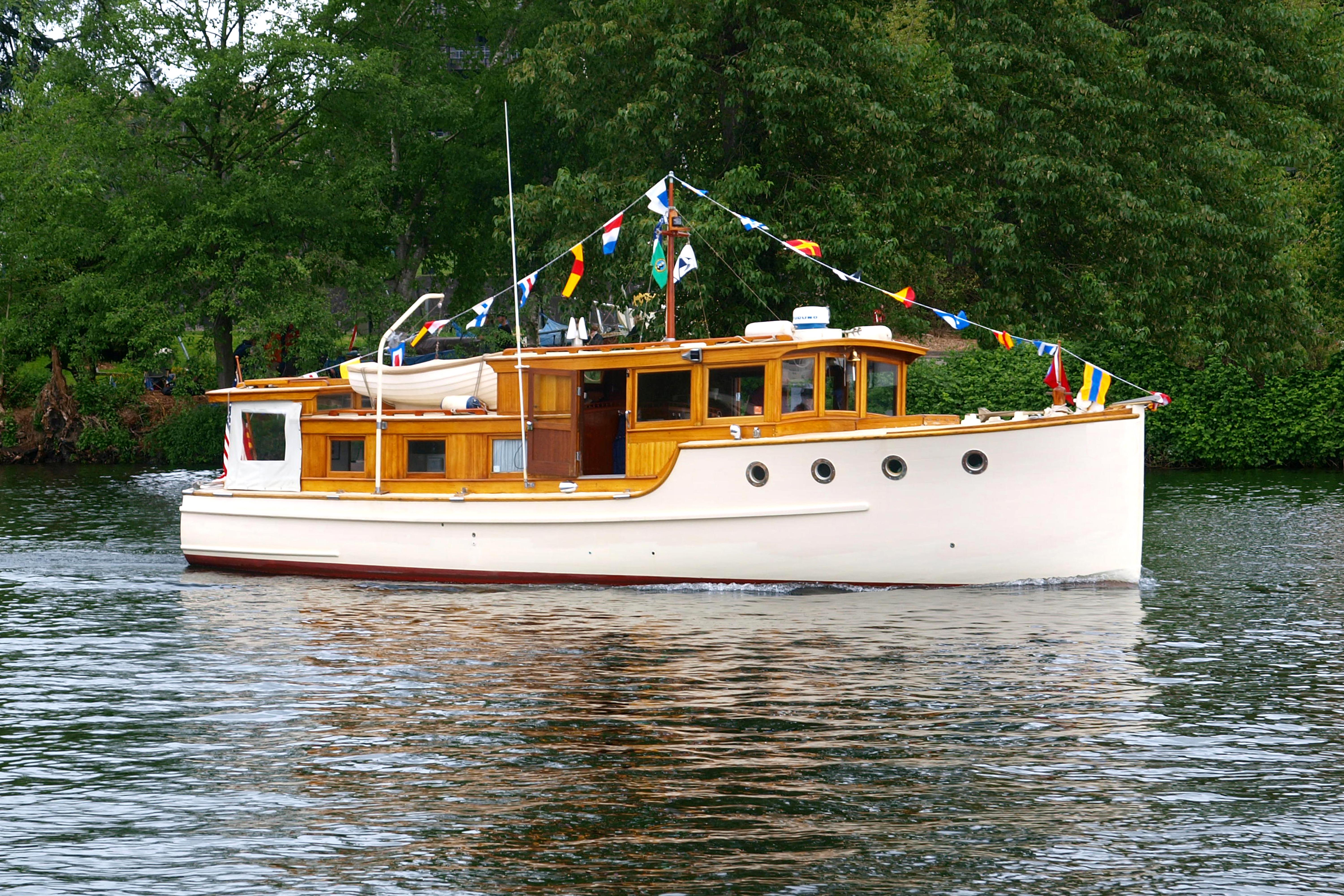 Vintage 1942 Grenfell 42 Custom boat adorned with colorful flags on a serene lake.
