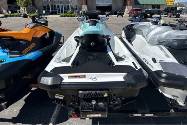 Three jet skis are parked on a trailer in a parking lot.