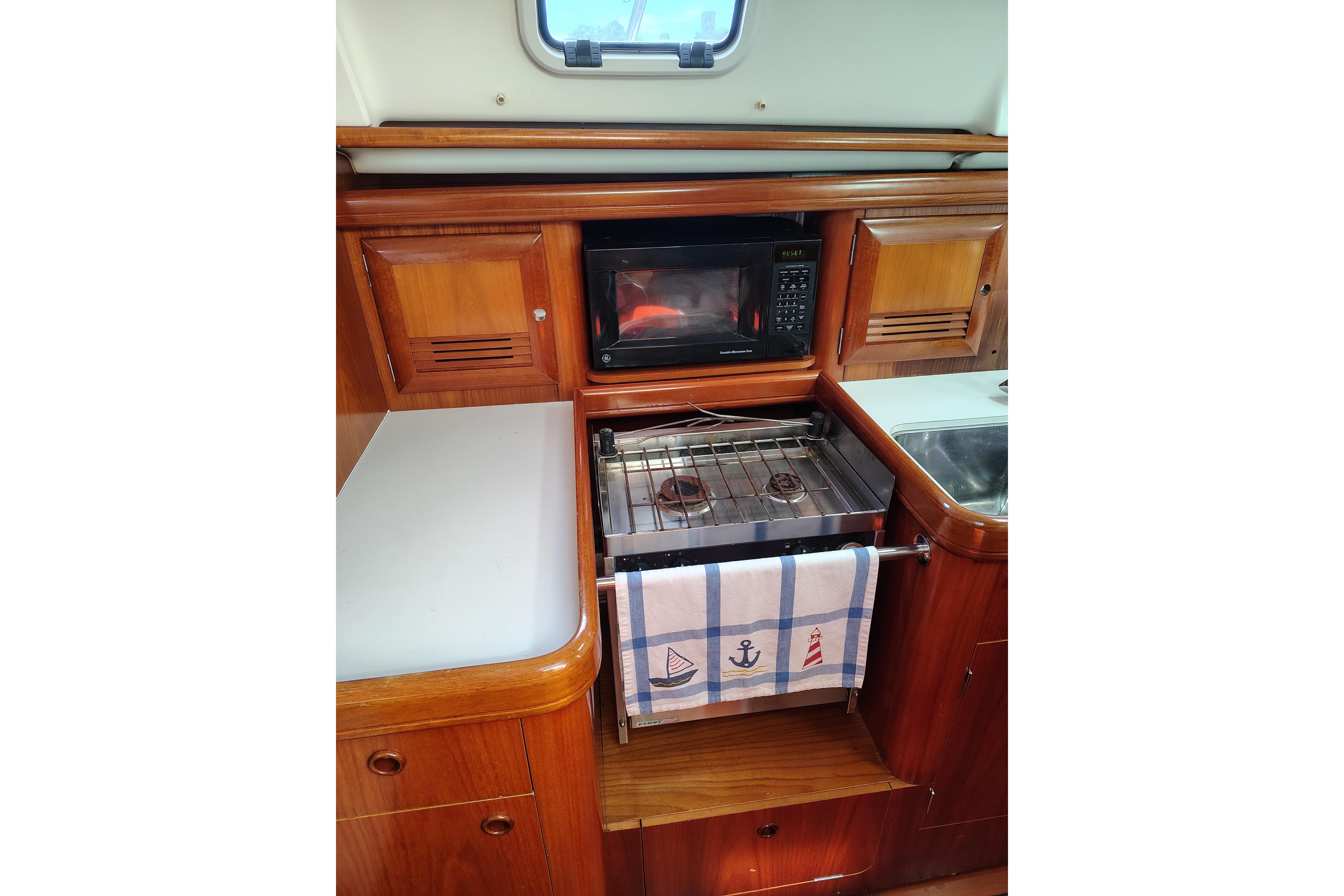 Galley kitchen in 2001 Beneteau Oceanis 411 sailboat with stove, microwave, and wooden cabinetry.