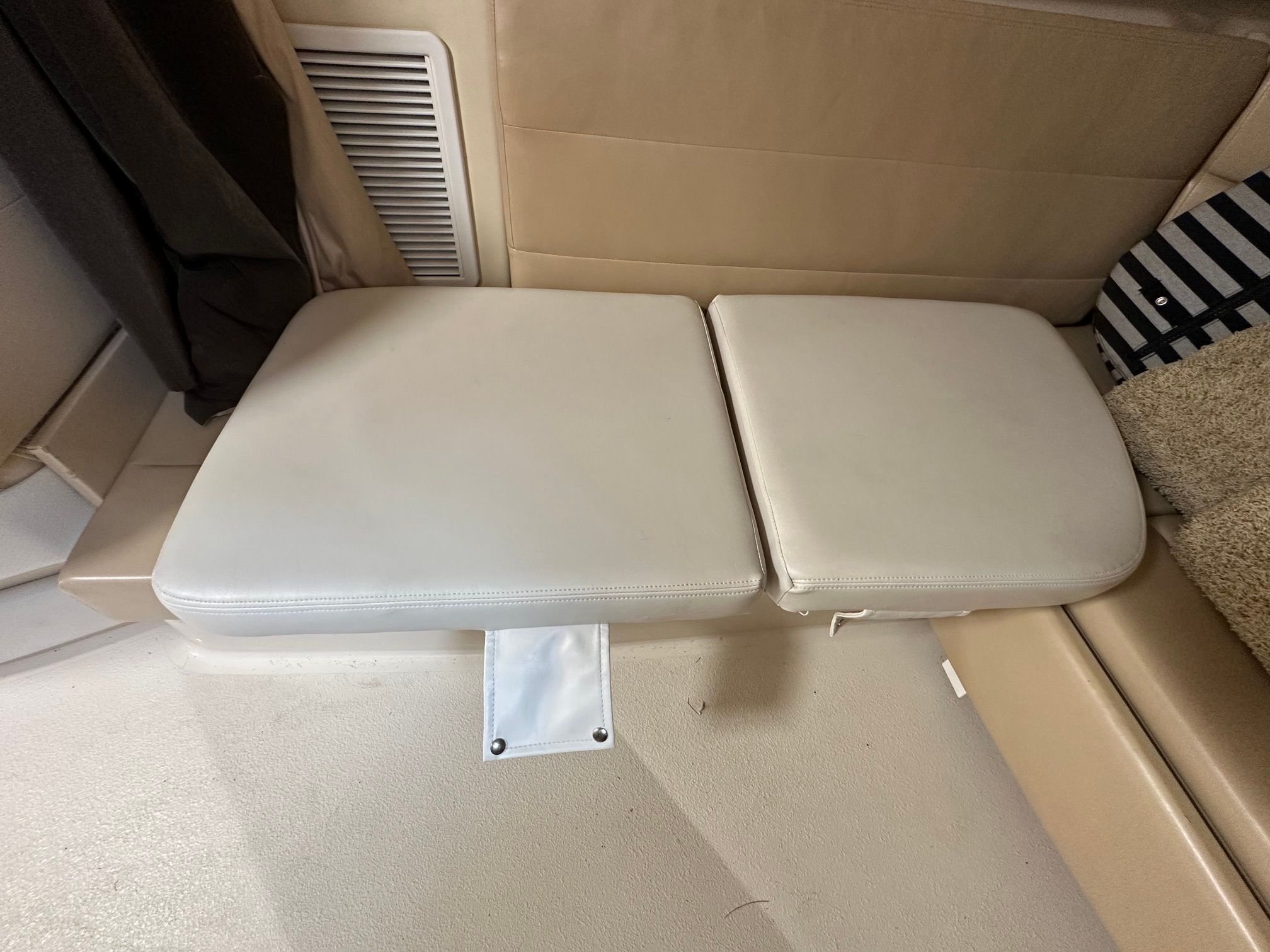 Beige seat cushions on a boat with a striped pillow and carpet.