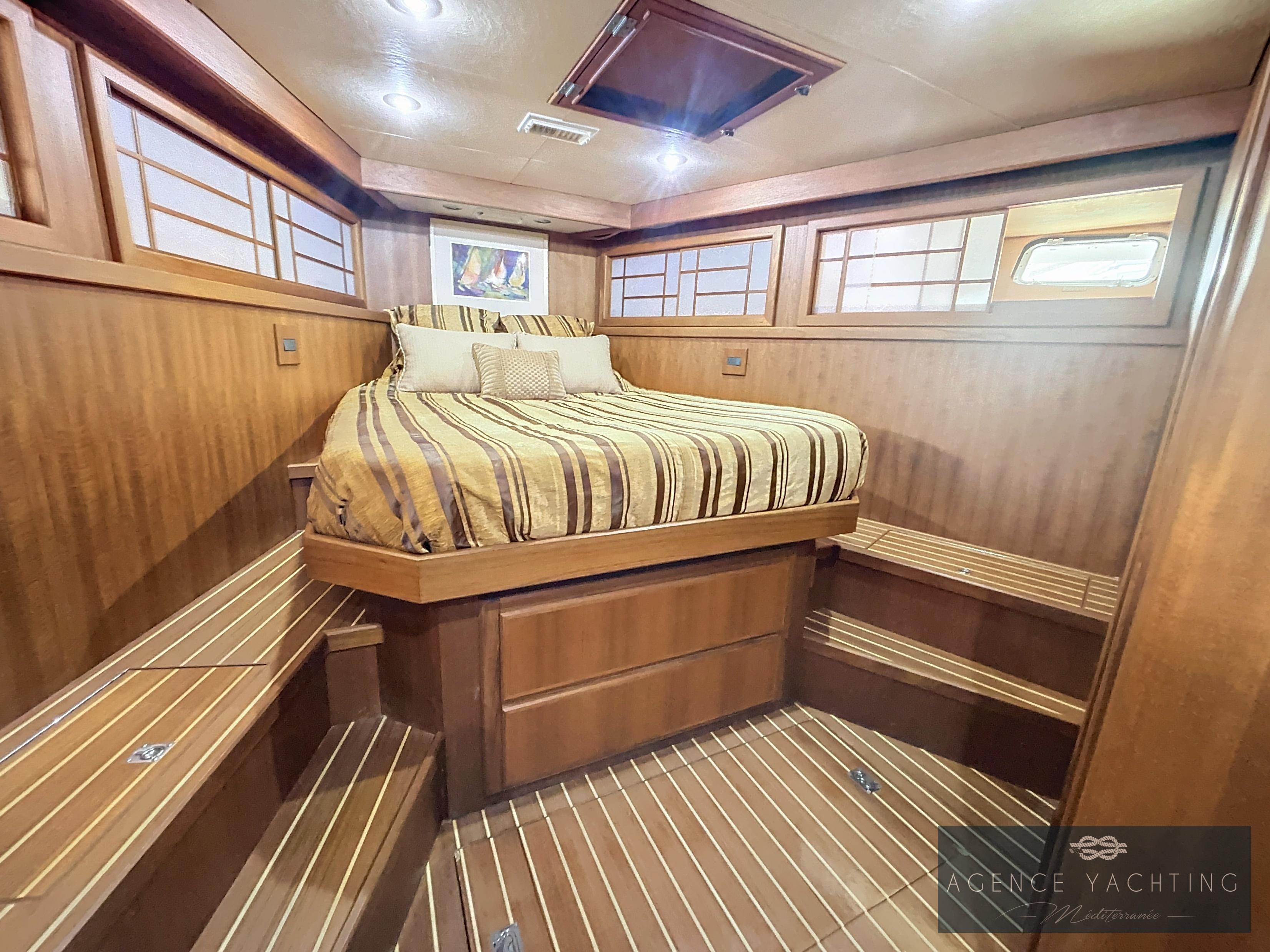 Luxurious 1987 Hatteras 85 yacht bedroom with wood paneling and striped bedding.