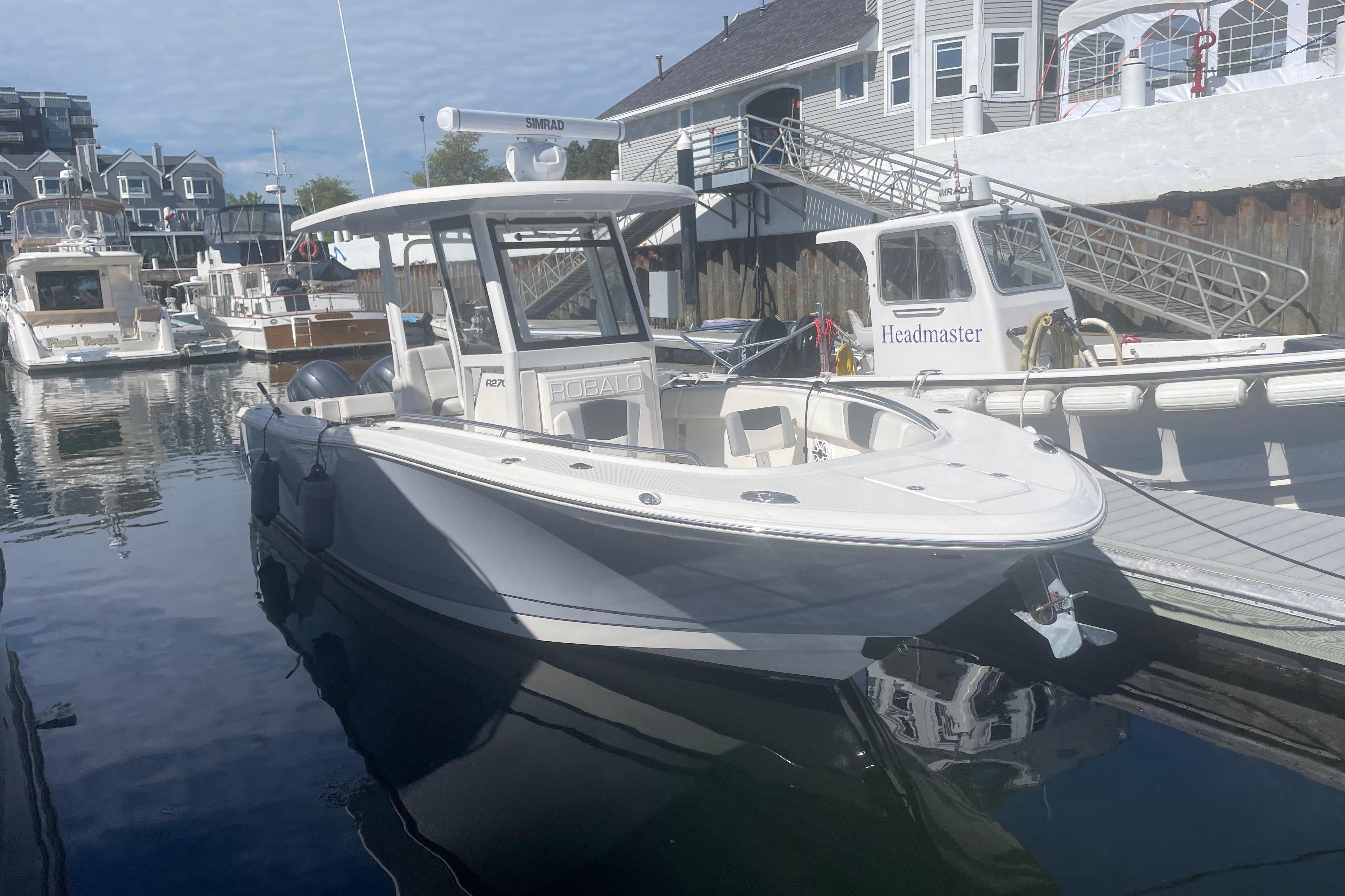 2023 Robalo R270 Center Console boat docked in a marina, surrounded by other vessels.