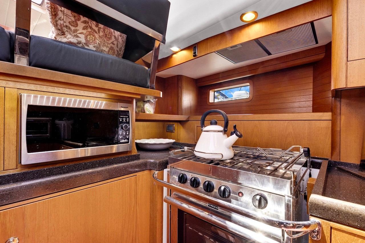 Luxurious 2011 Southerly 57 RS yacht kitchen with stove, microwave, and wooden cabinetry.