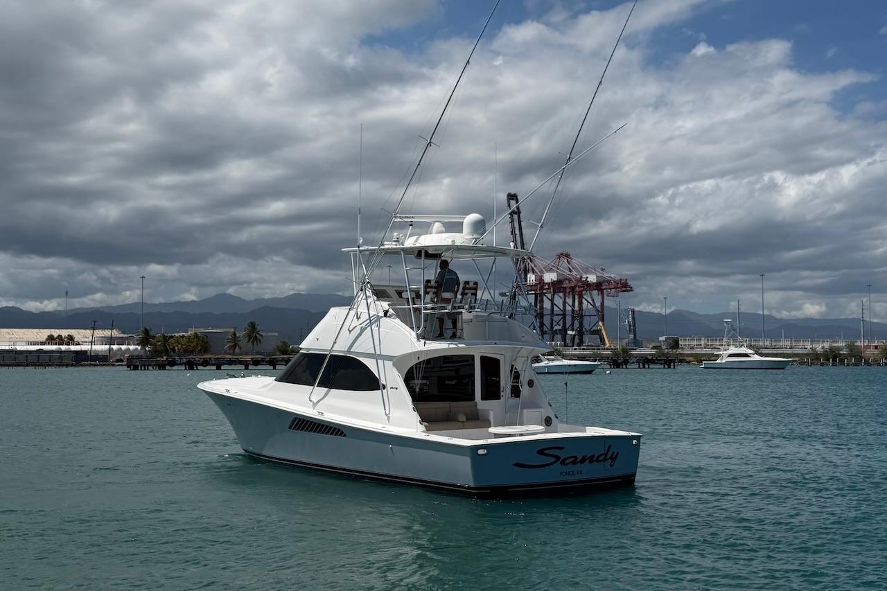 2012 Viking 50 Convertible yacht named "Sandy" on calm waters near a port.