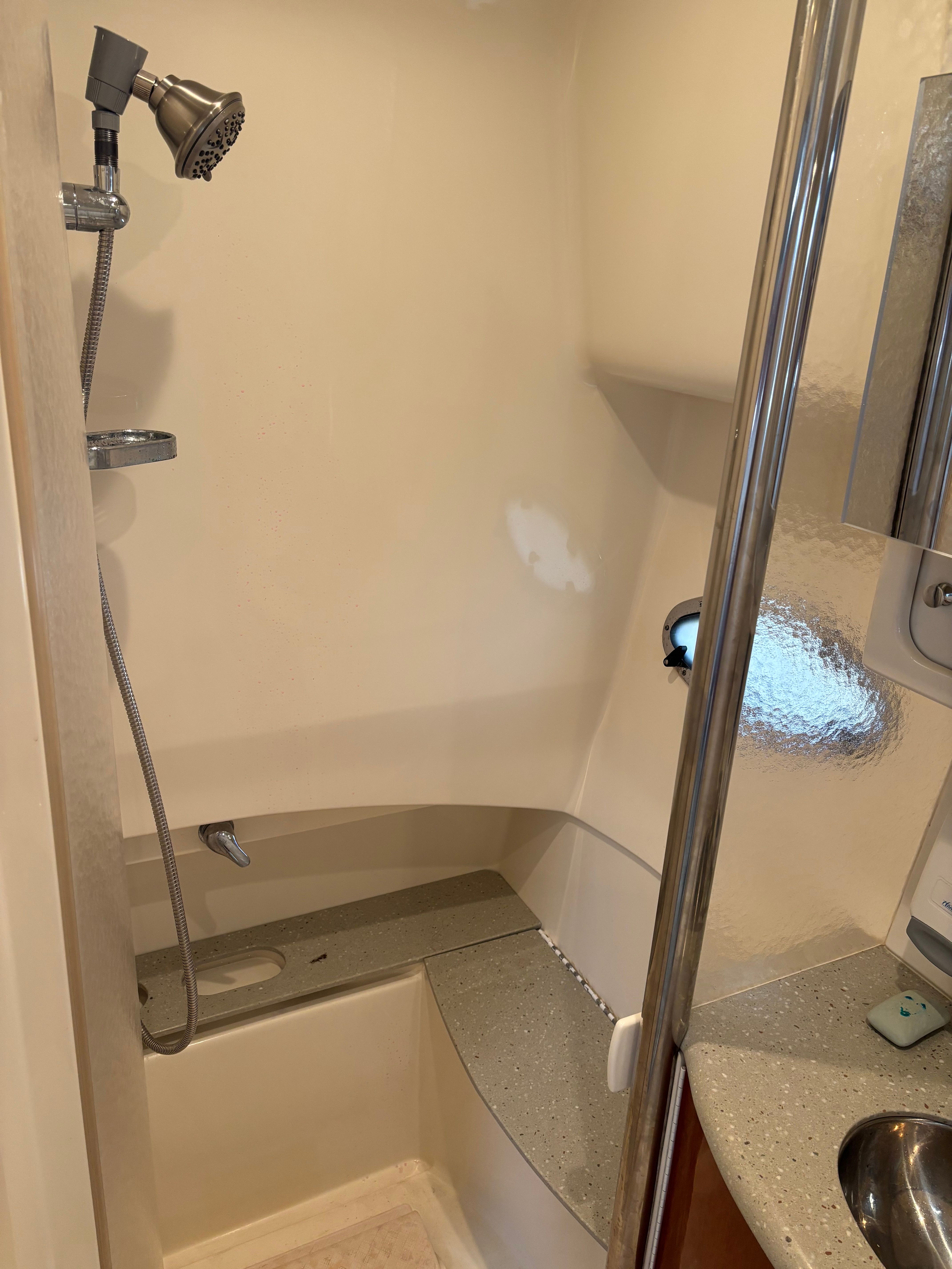 Shower in a boat cabin with handheld showerhead and sink.
