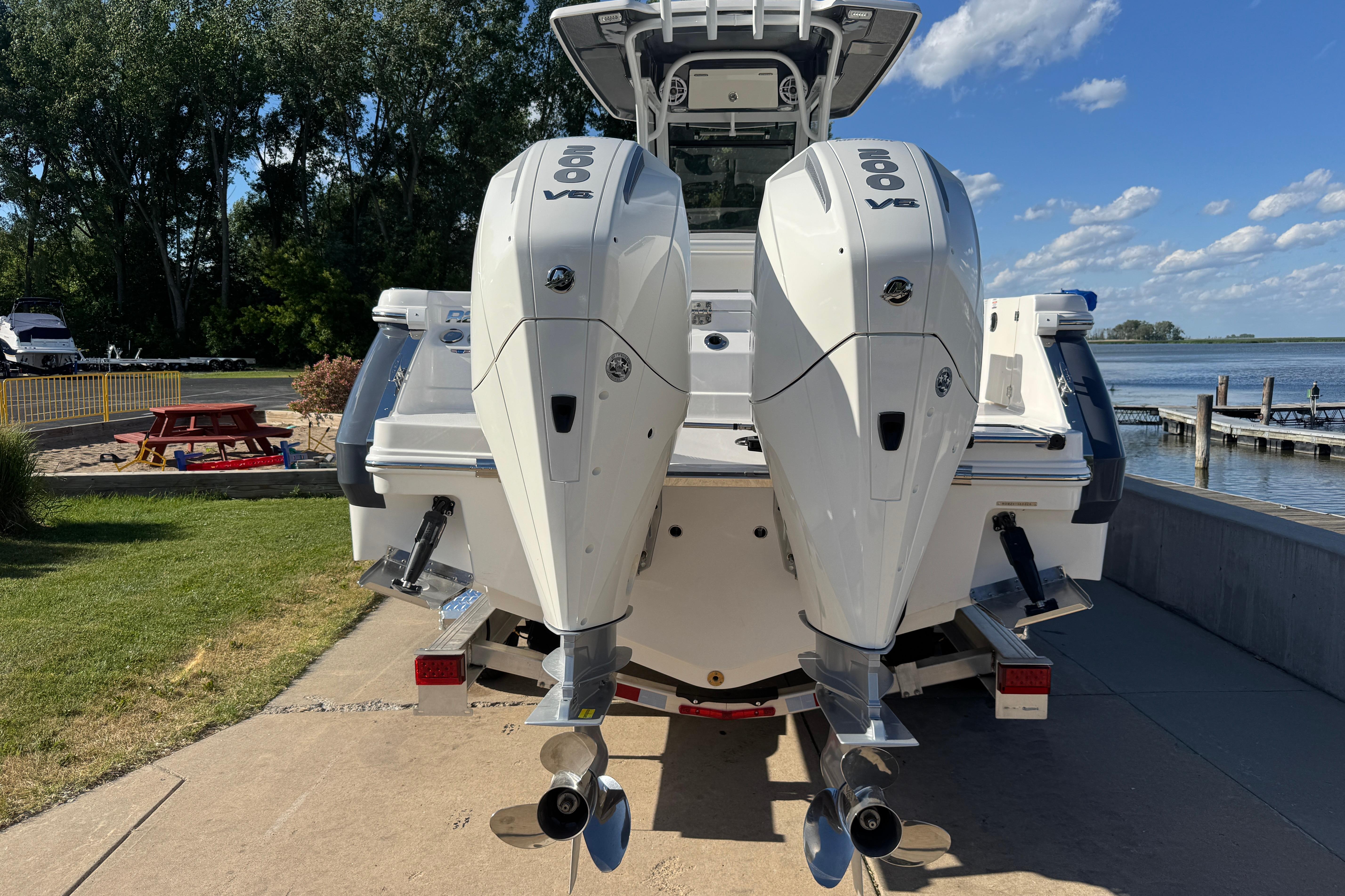 2026 Robalo R250 Center Console boat with dual outboard engines, docked by a scenic lake.