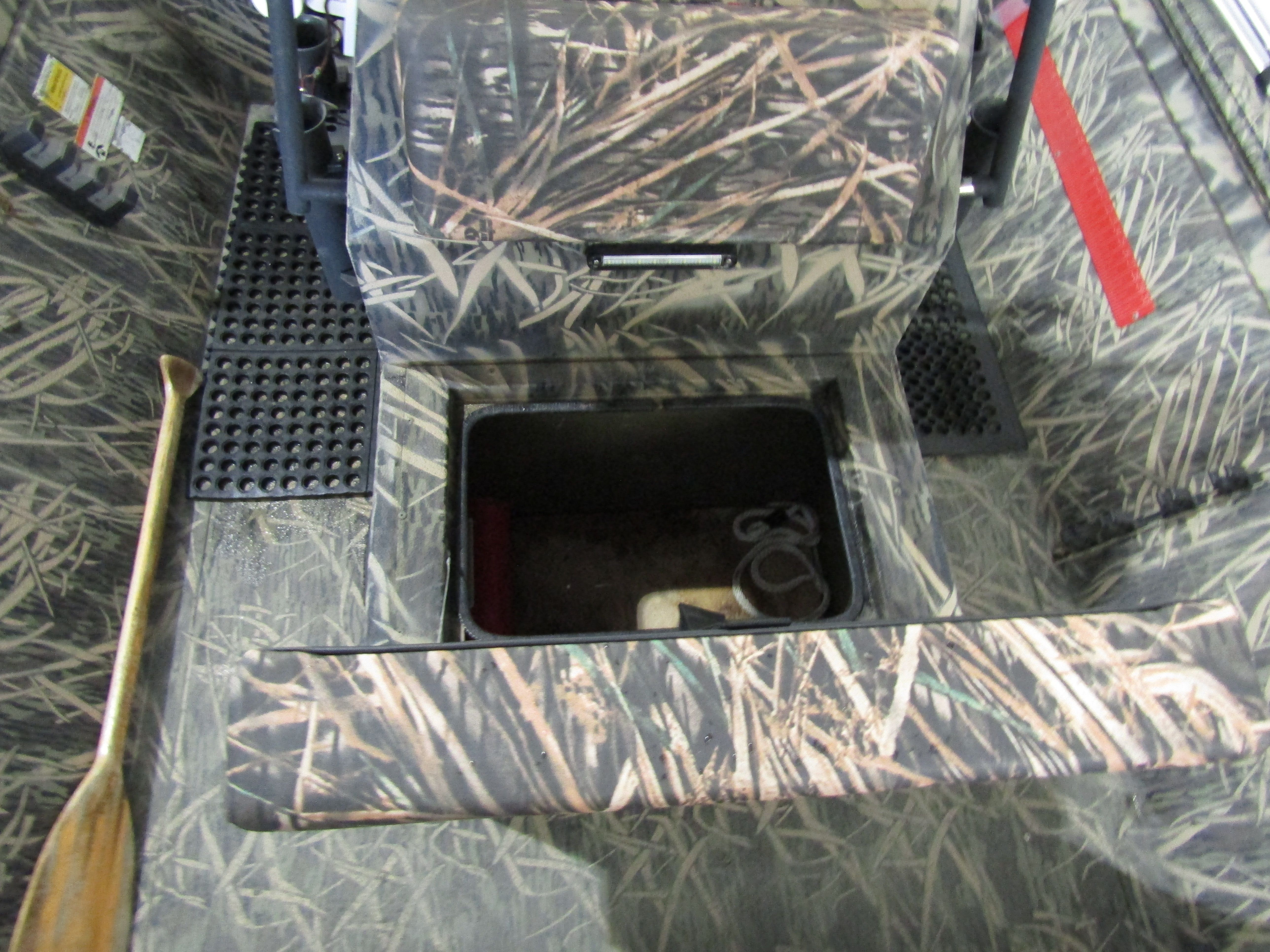 The image shows a boat interior with an open storage compartment and a paddle.