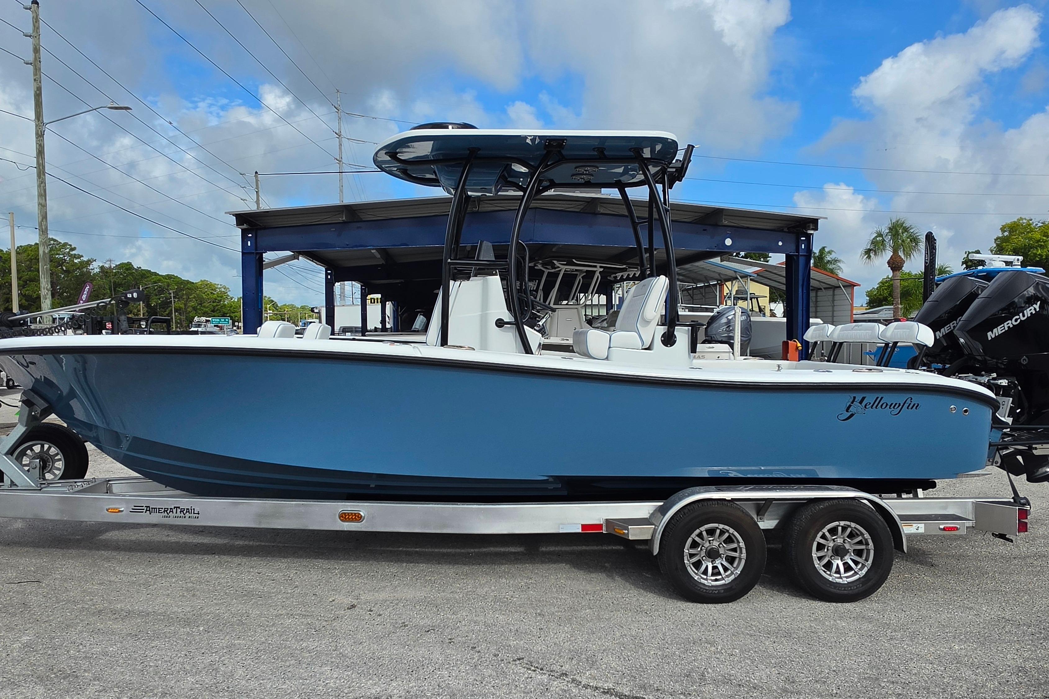2025 Yellowfin 26 Hybrid boat on trailer, blue hull, parked outdoors under cloudy sky.