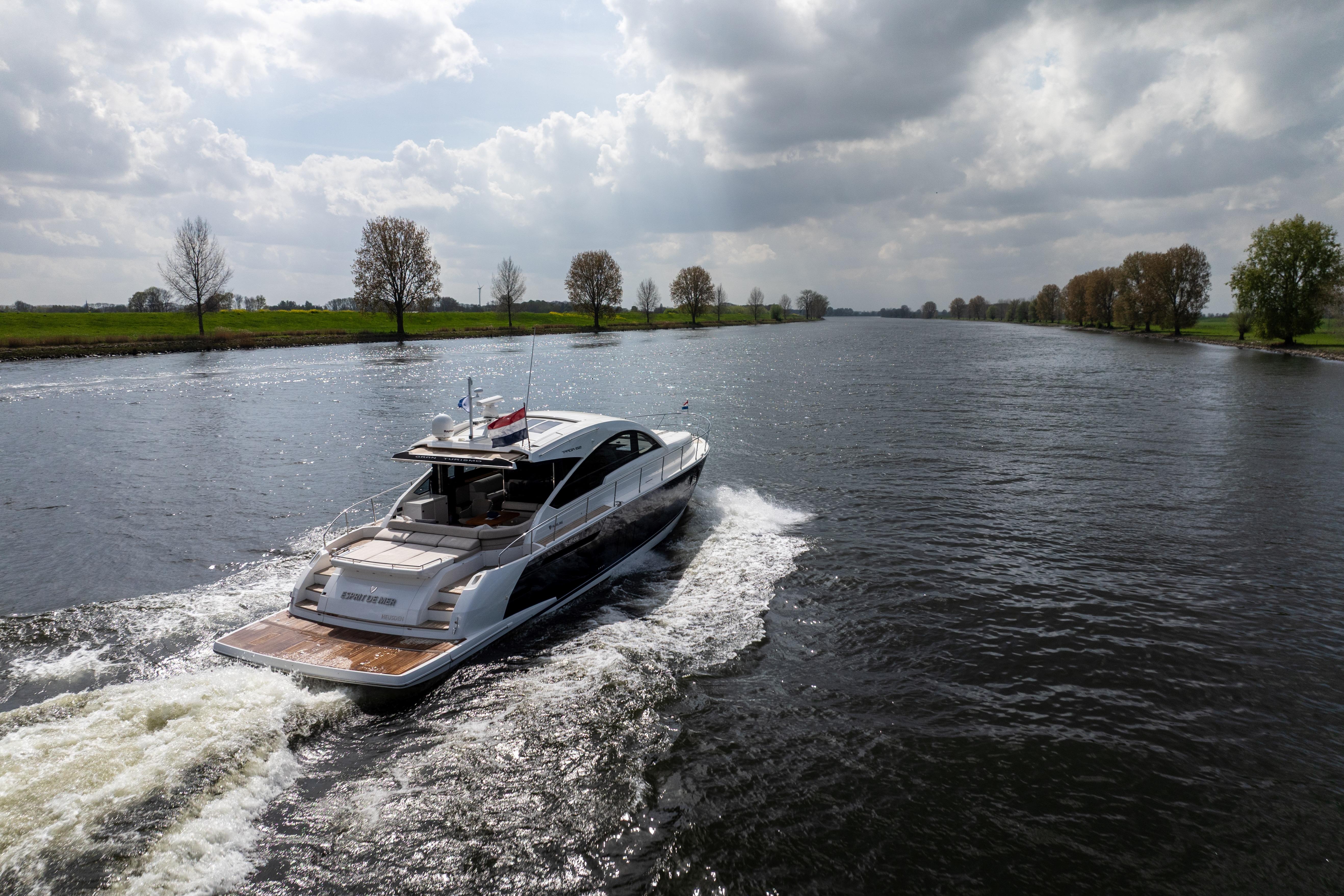 2015 Fairline Targa 62 GT yacht cruising on a scenic river under cloudy skies.