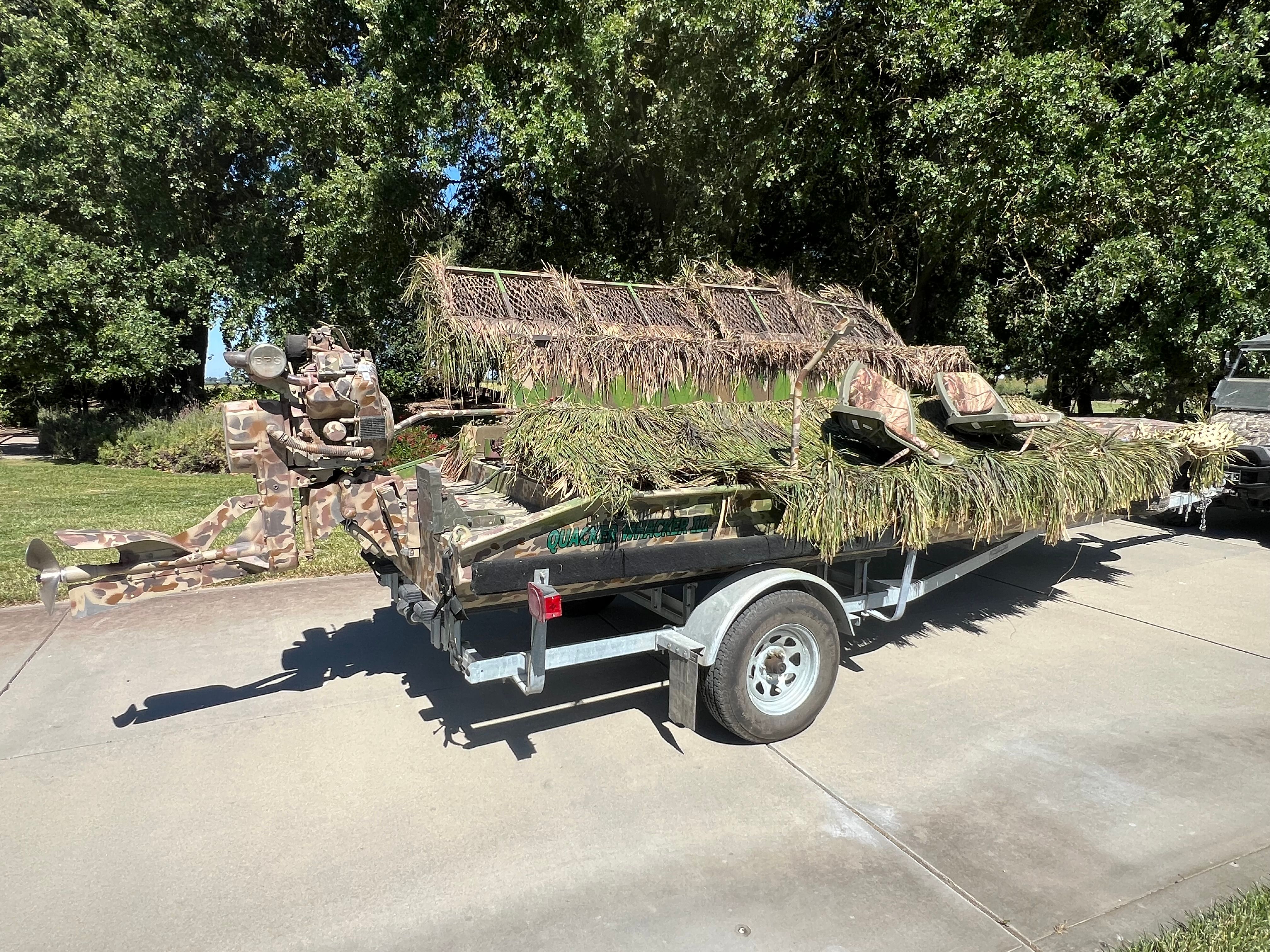 A 2016 Gator Trax 18 X 54 boat with camouflage on a trailer, surrounded by trees.